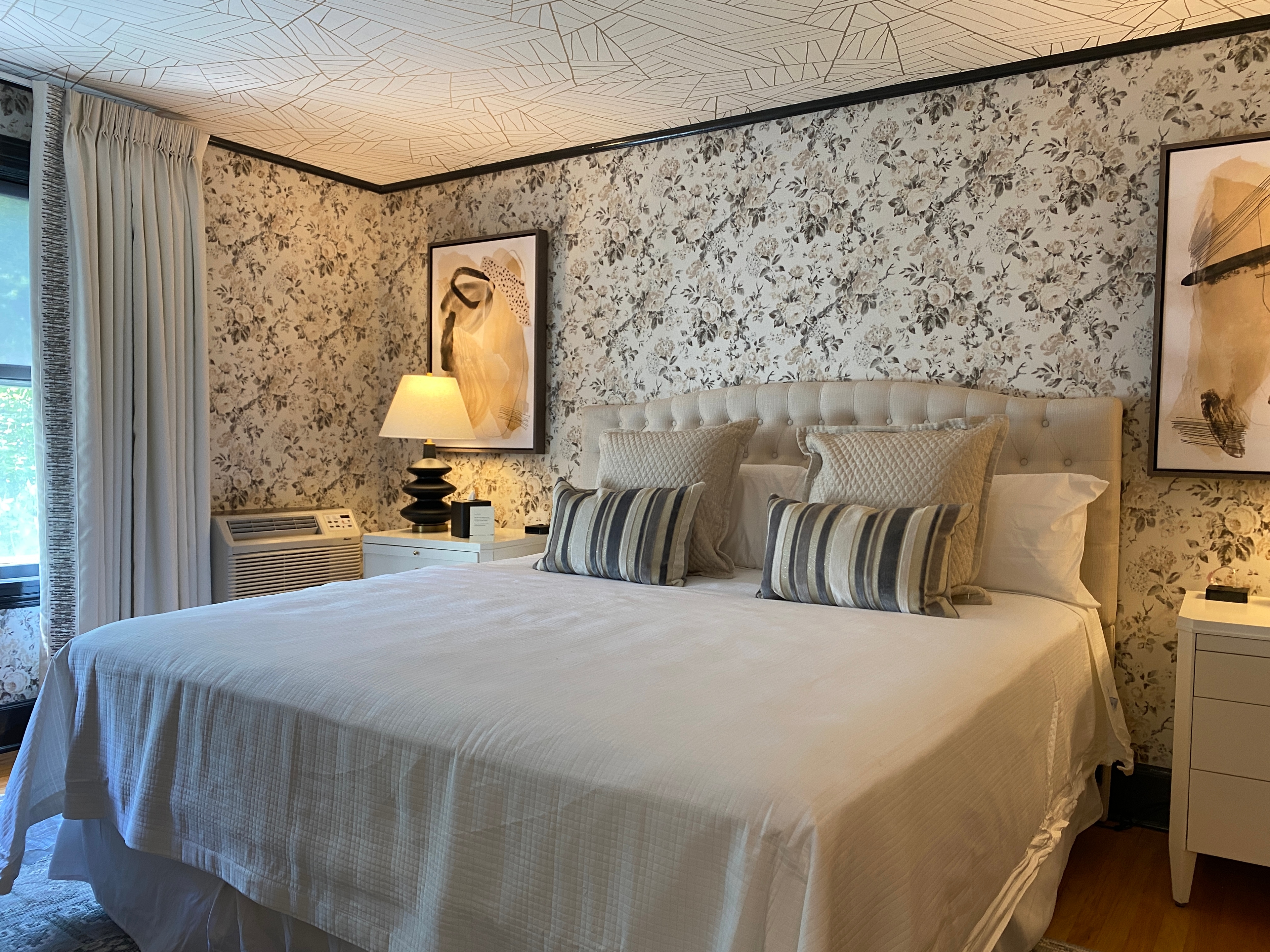 A bedroom with floral wallpaper, a patterned ceiling, and a made bed with pillows.