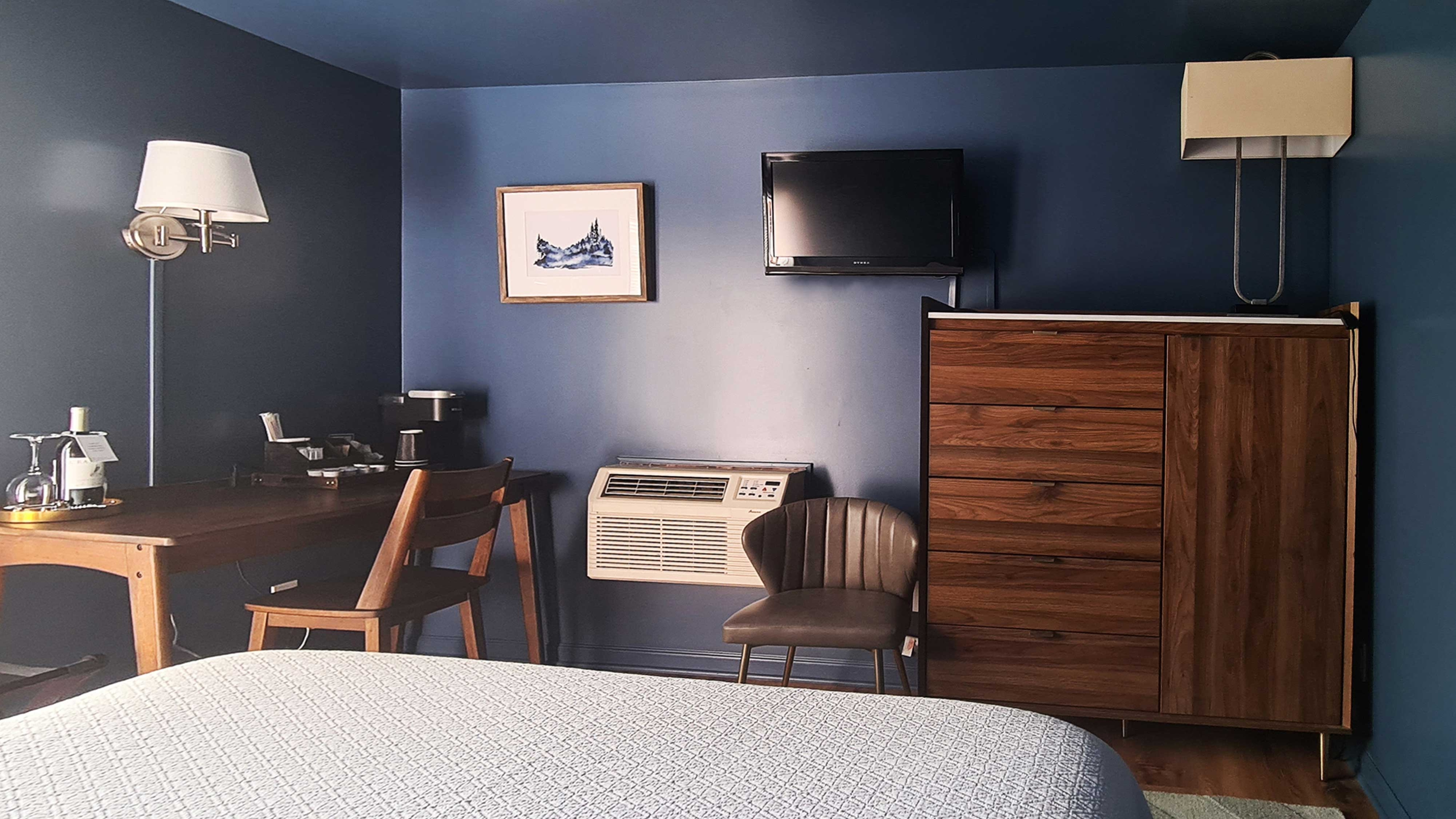 A hotel room with a desk, two chairs, a TV, a dresser, and two lamps.