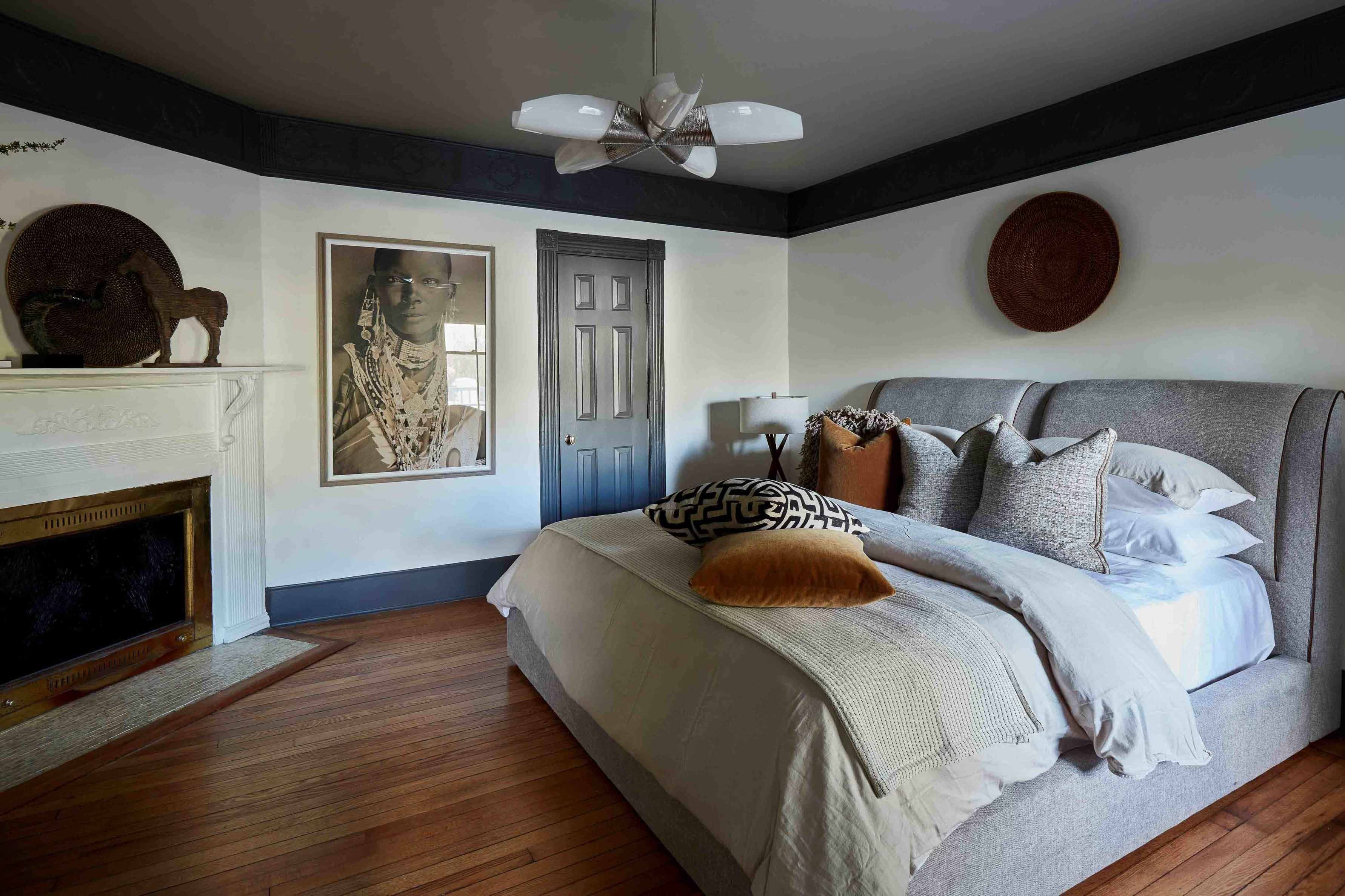 Bedroom with a gray upholstered bed, fireplace, and artwork.