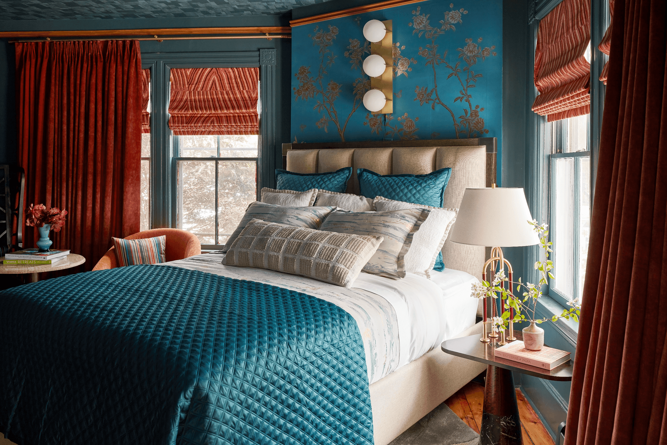 A bedroom with a blue and gold color scheme, a bed, and two windows.