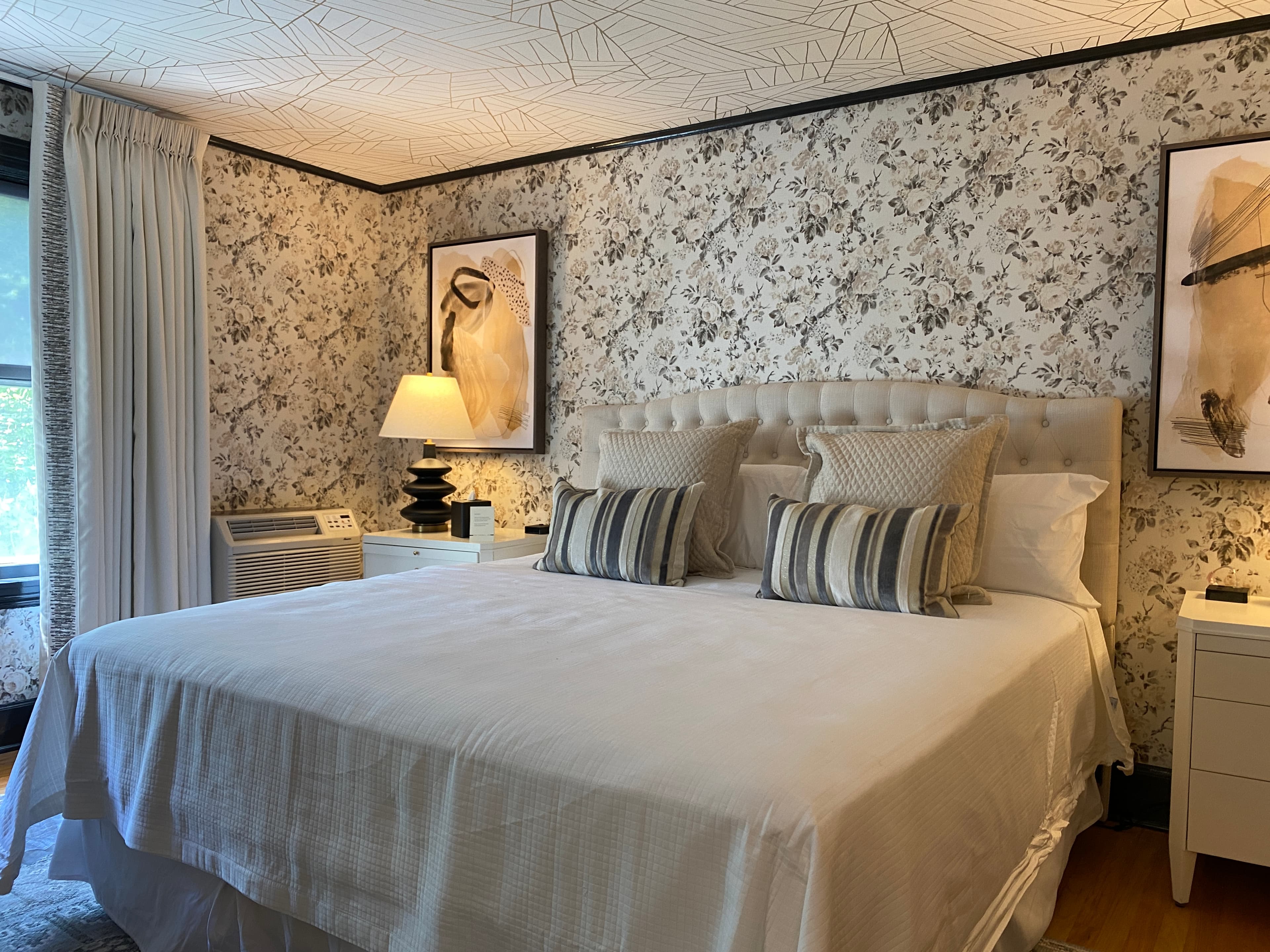 A bedroom with floral wallpaper, a patterned ceiling, and a made bed with pillows.
