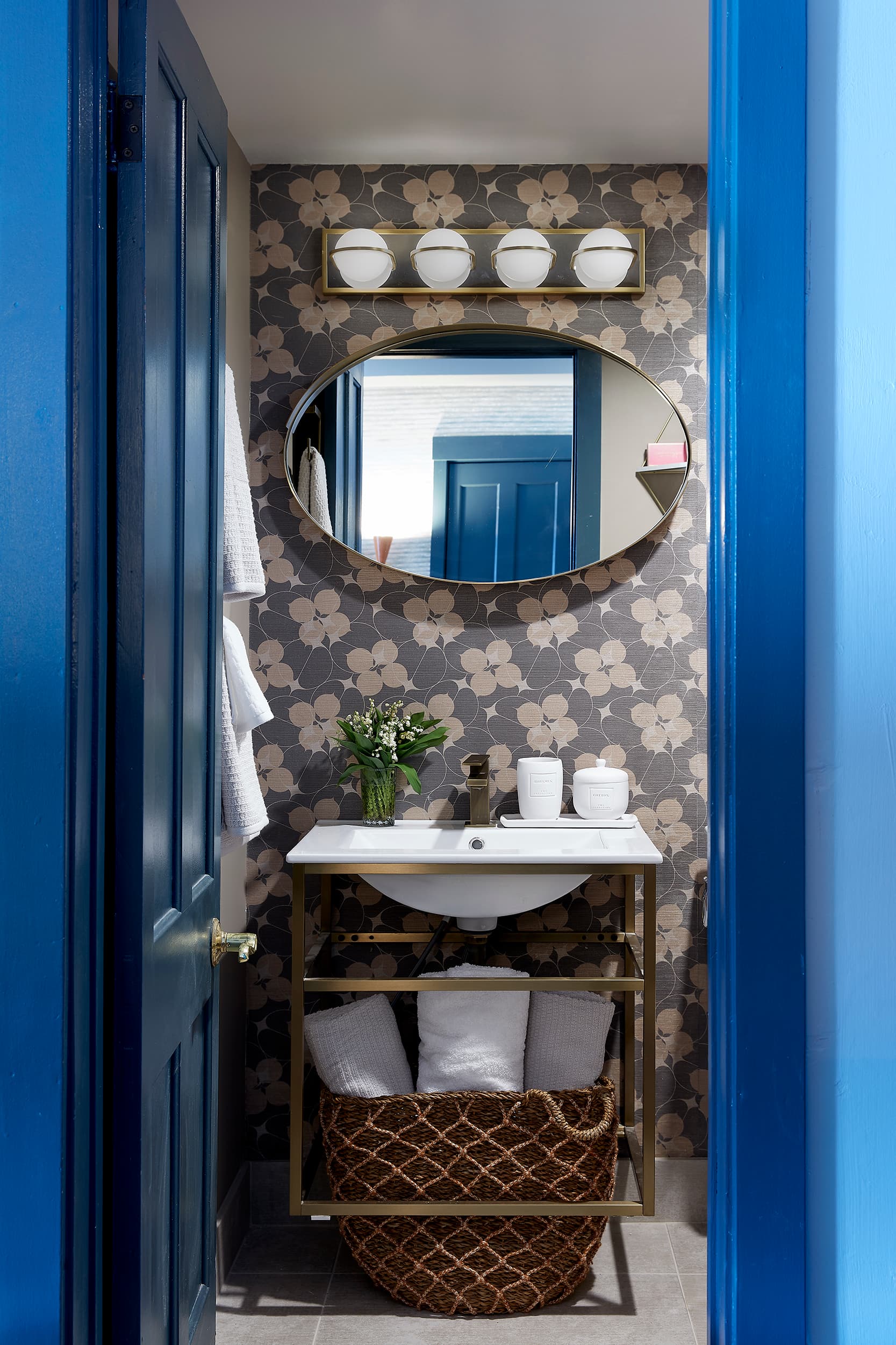 A small bathroom with floral wallpaper, a sink, and a blue door.