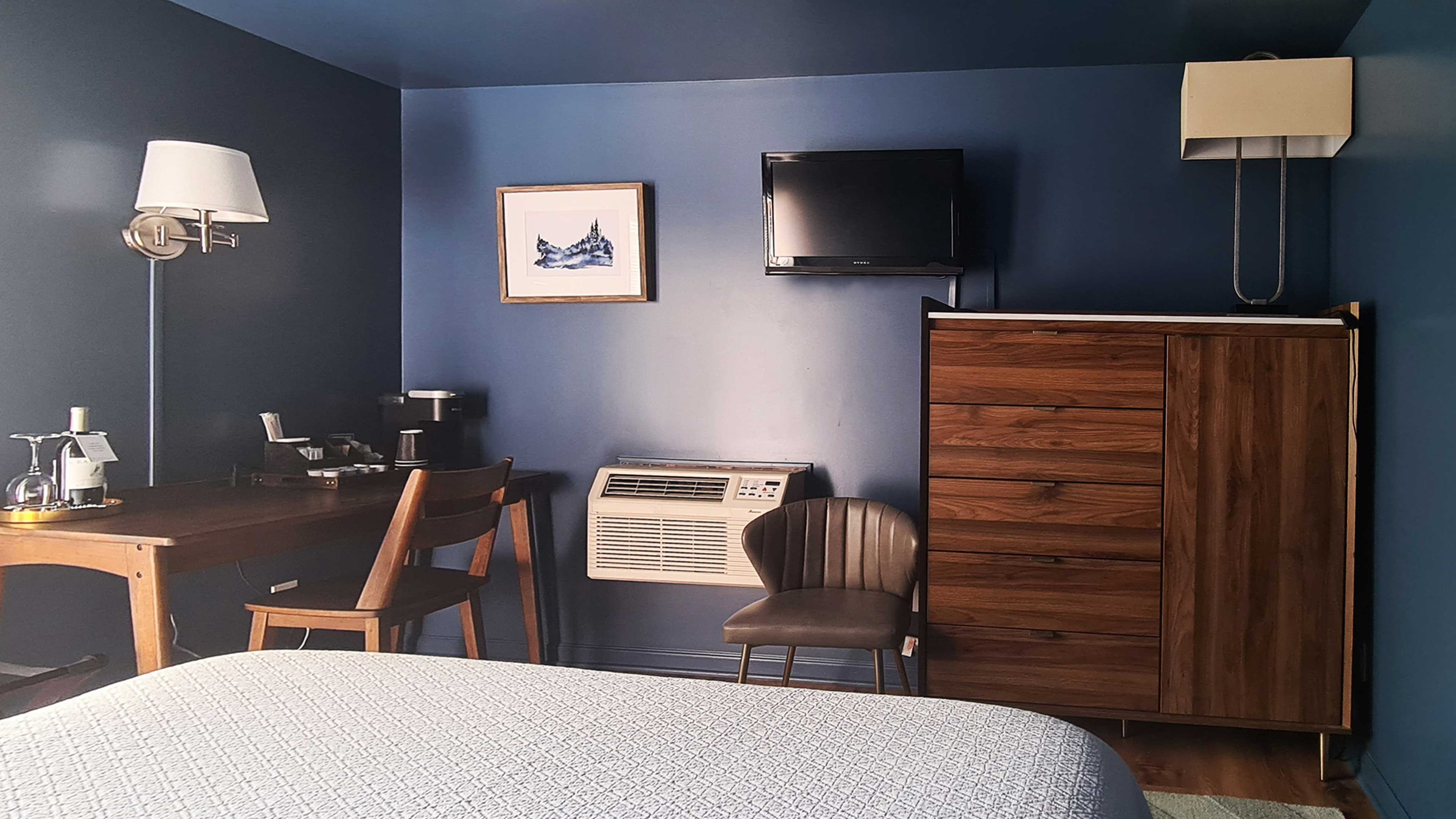 A hotel room with a desk, two chairs, a TV, a dresser, and two lamps.