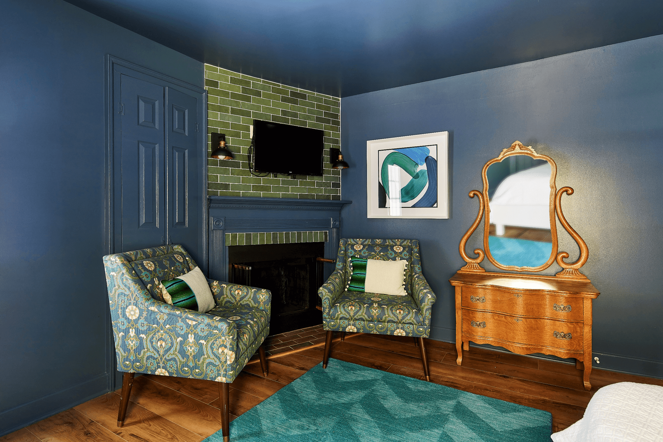 A sitting area with two patterned armchairs, a fireplace, and a wooden dresser with a mirror.