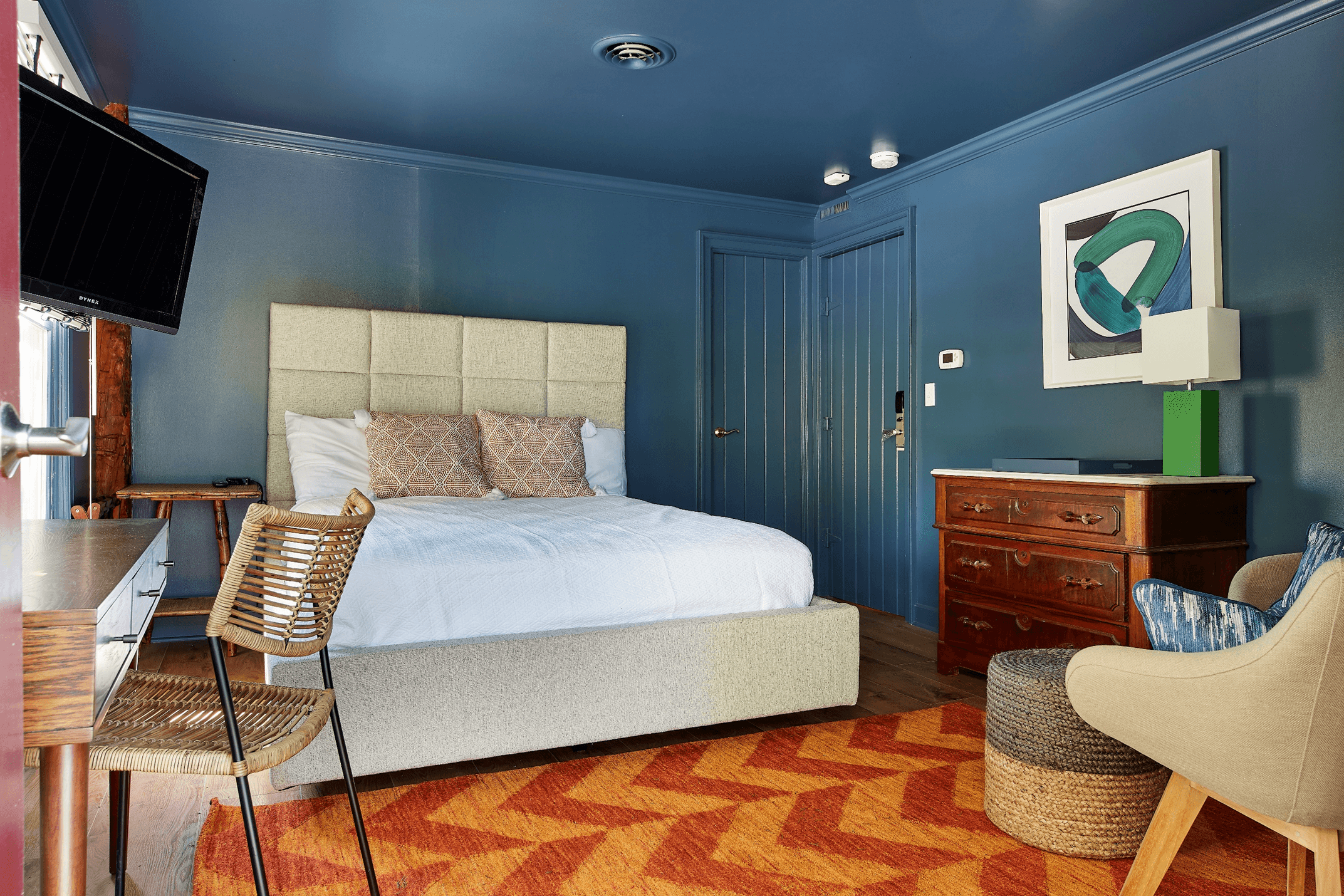 A blue bedroom with a made bed, a desk, a chair, and a dresser.