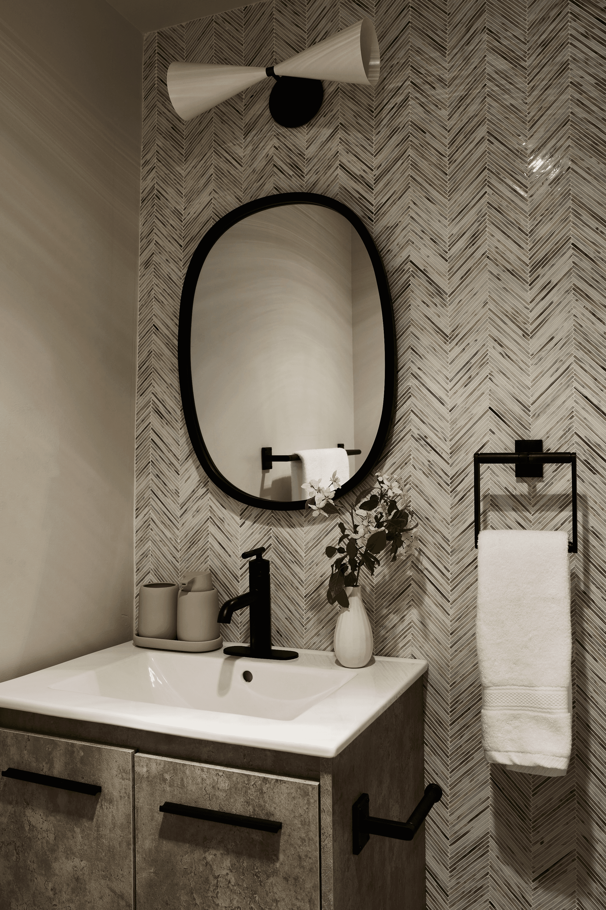 A bathroom sink with a black oval mirror, a light fixture, and a towel.
