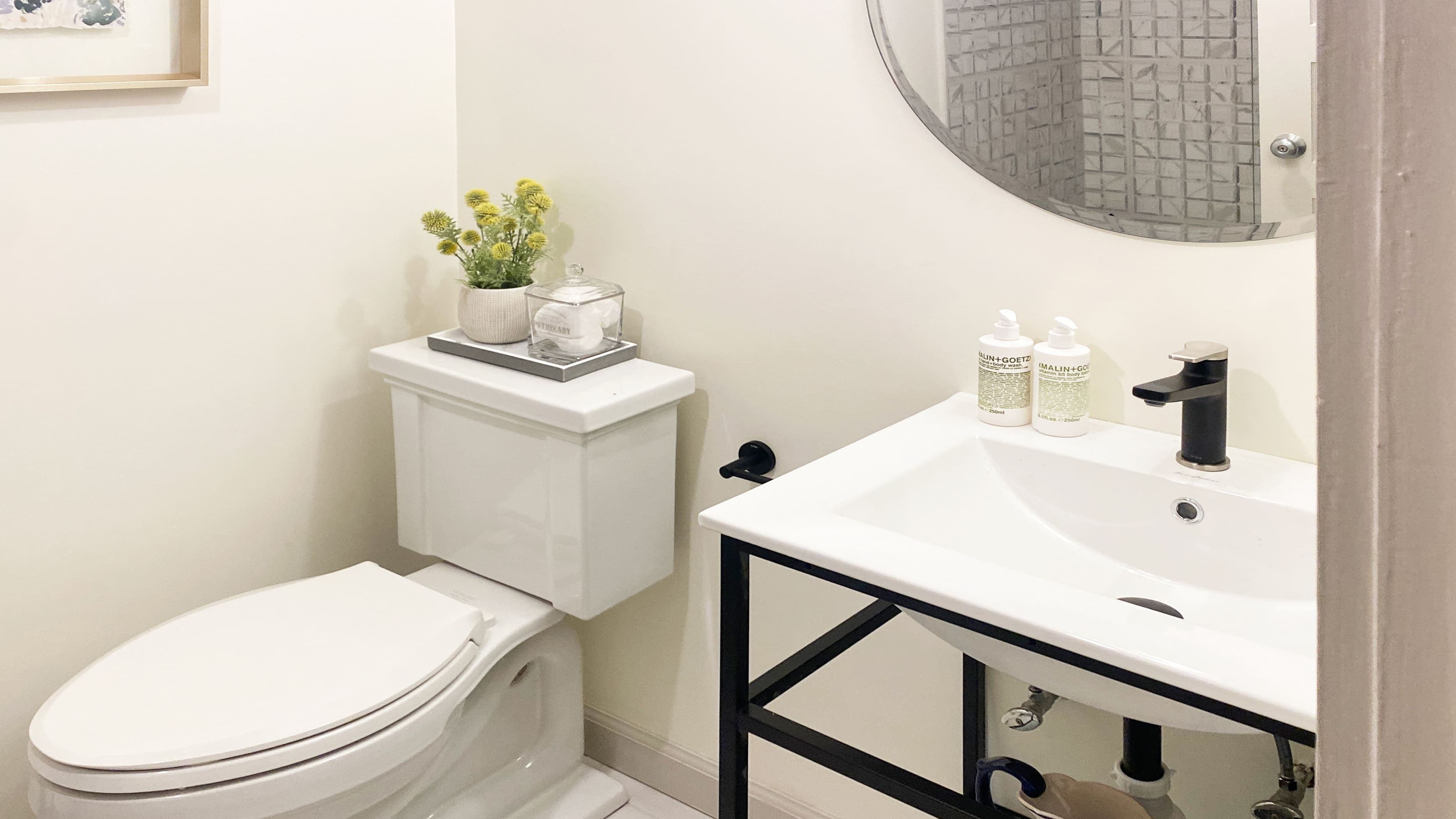 A bathroom with a toilet, sink, mirror, and floral arrangement.