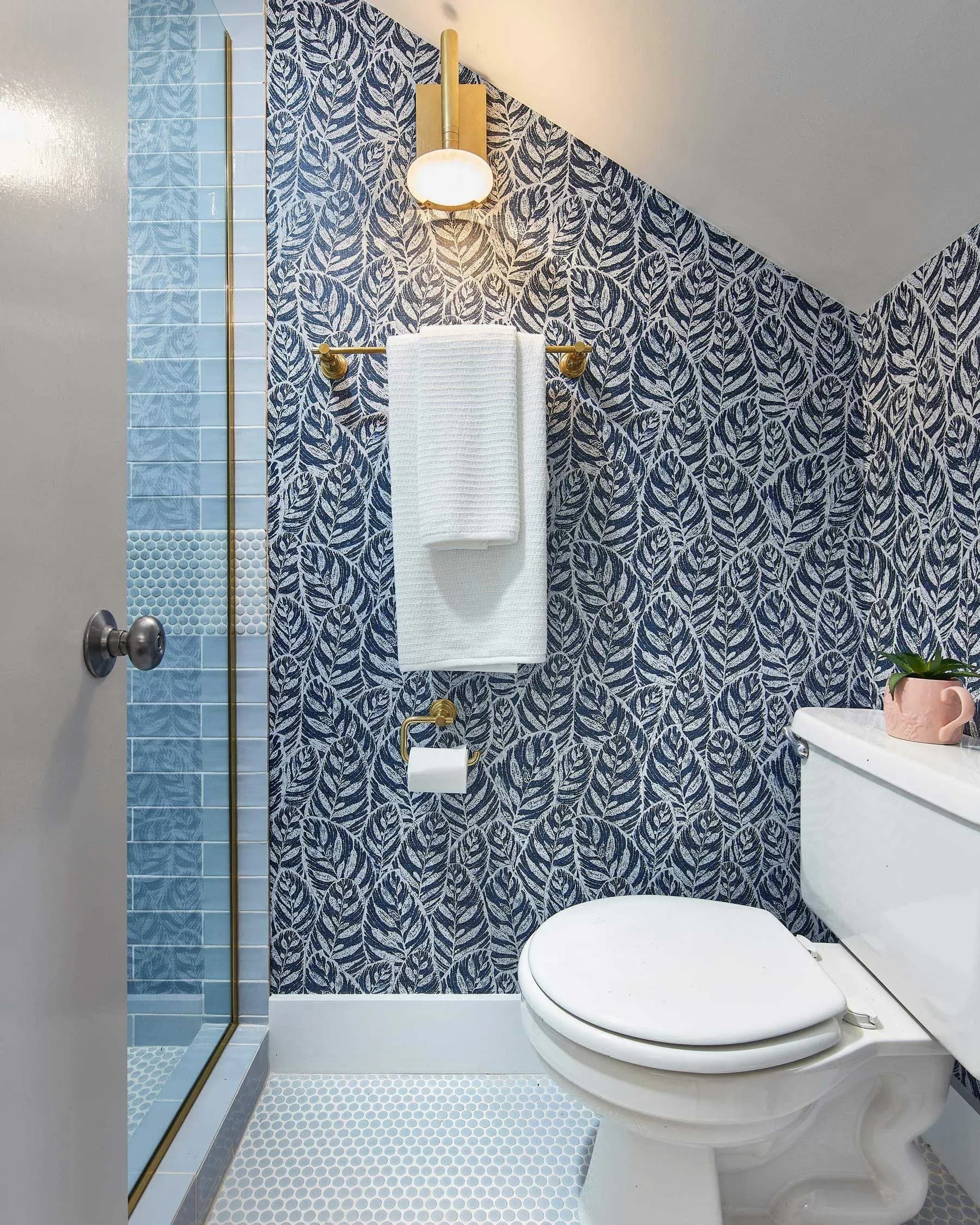 Small, stylish bathroom with leaf-patterned wallpaper and blue tiled shower.