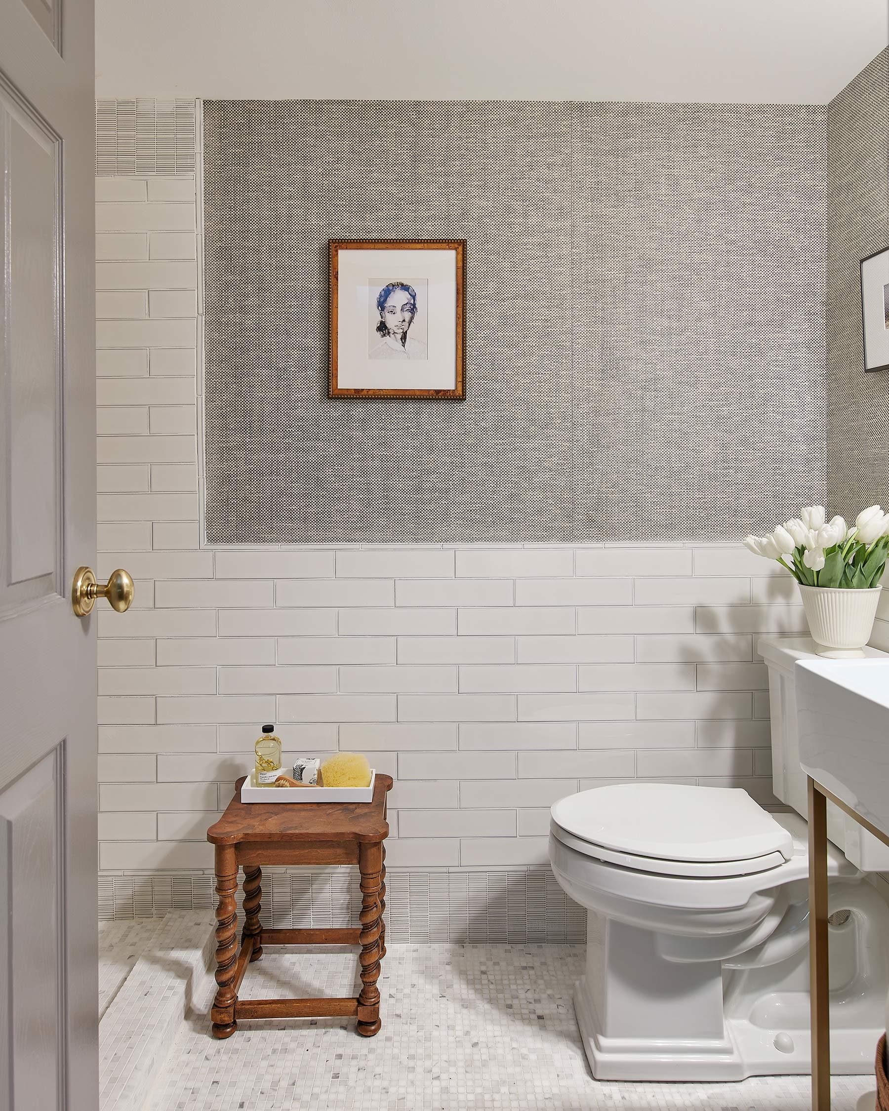 A small bathroom with a toilet, a wooden stool, and a framed picture.
