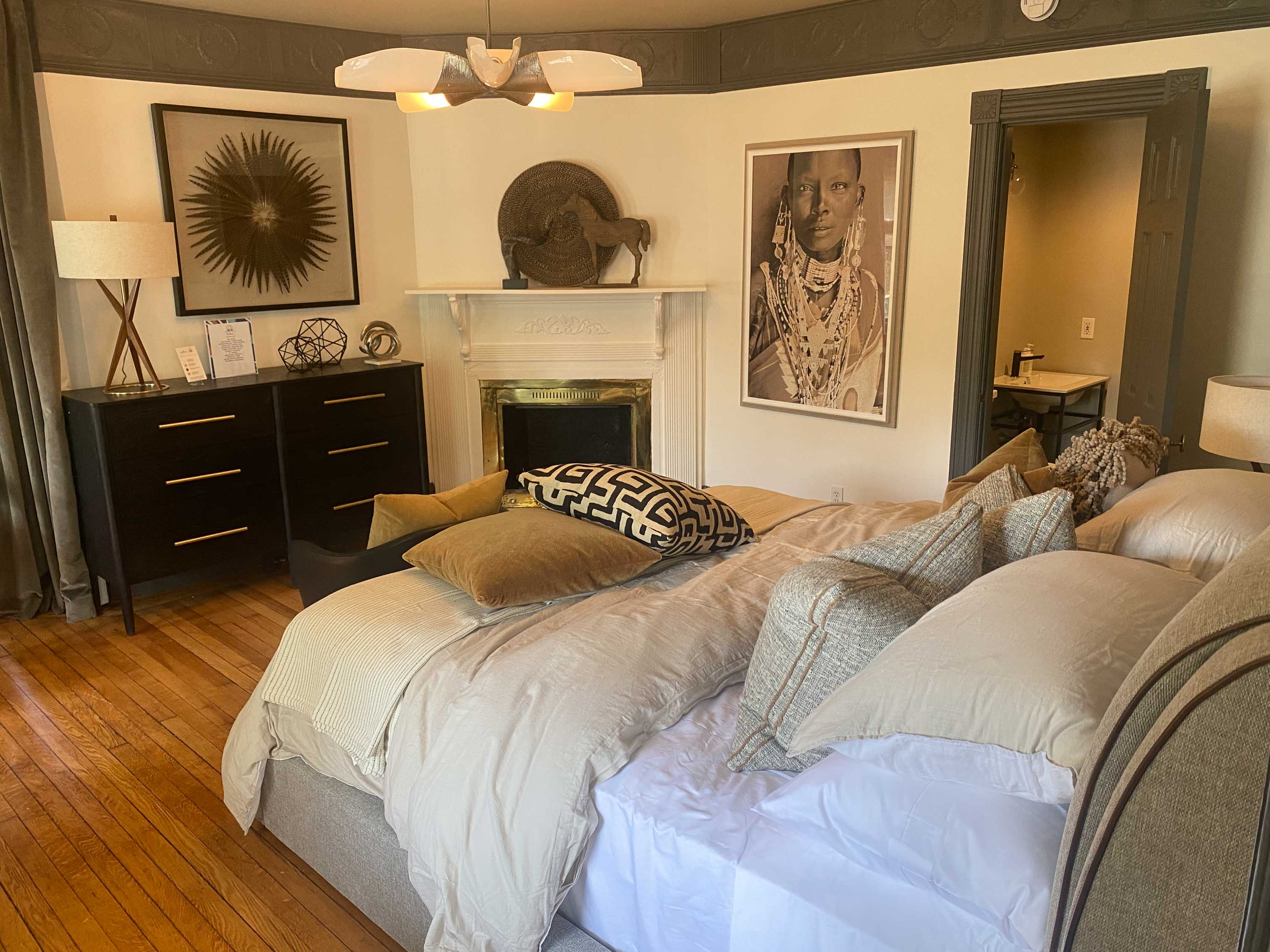 Another view of the Bedroom with a gray upholstered bed, fireplace, and artwork.