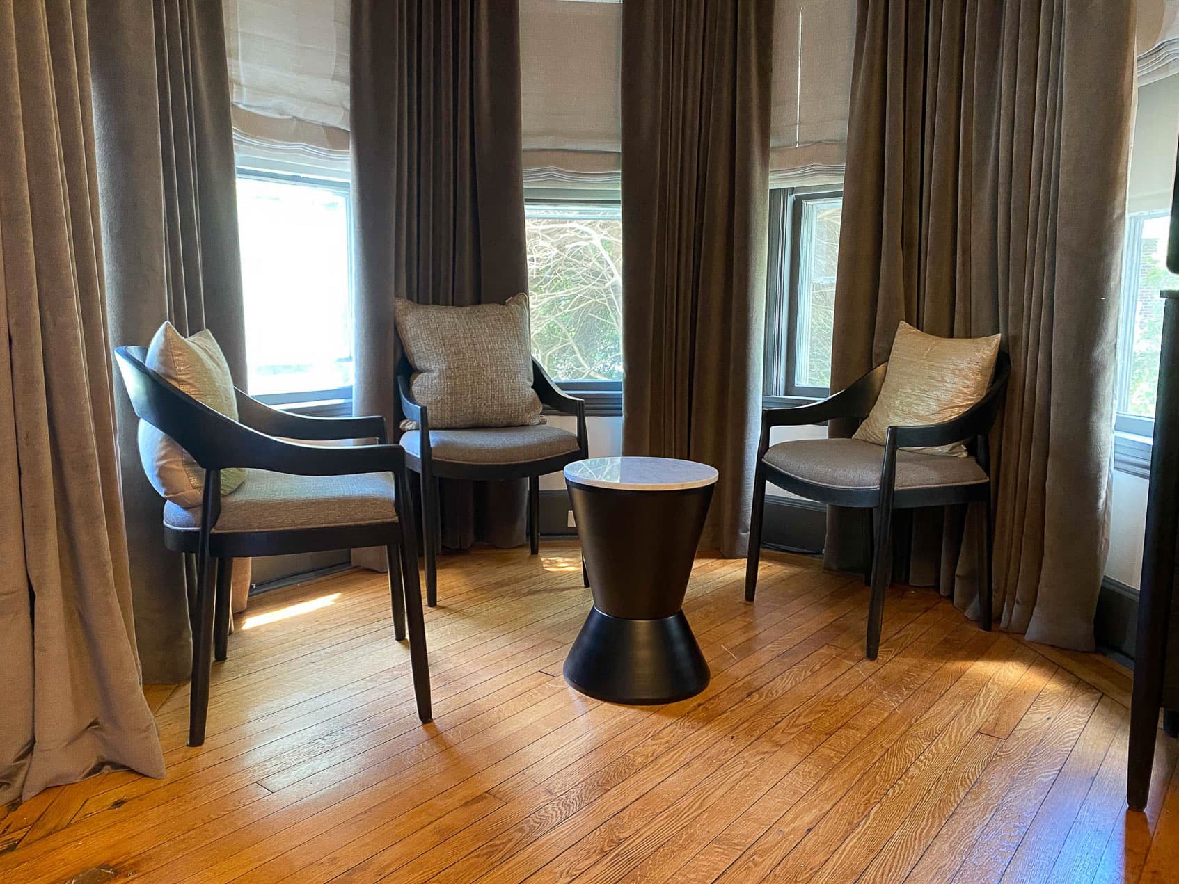 Three chairs arranged around a small table in a room with large windows and curtains.