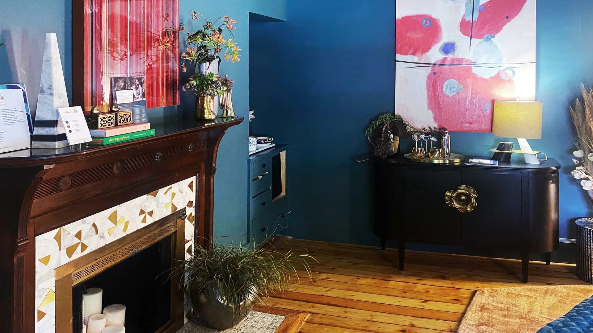 a decorated fireplace, bold artwork, and a stylish black cabinet with gold accents.