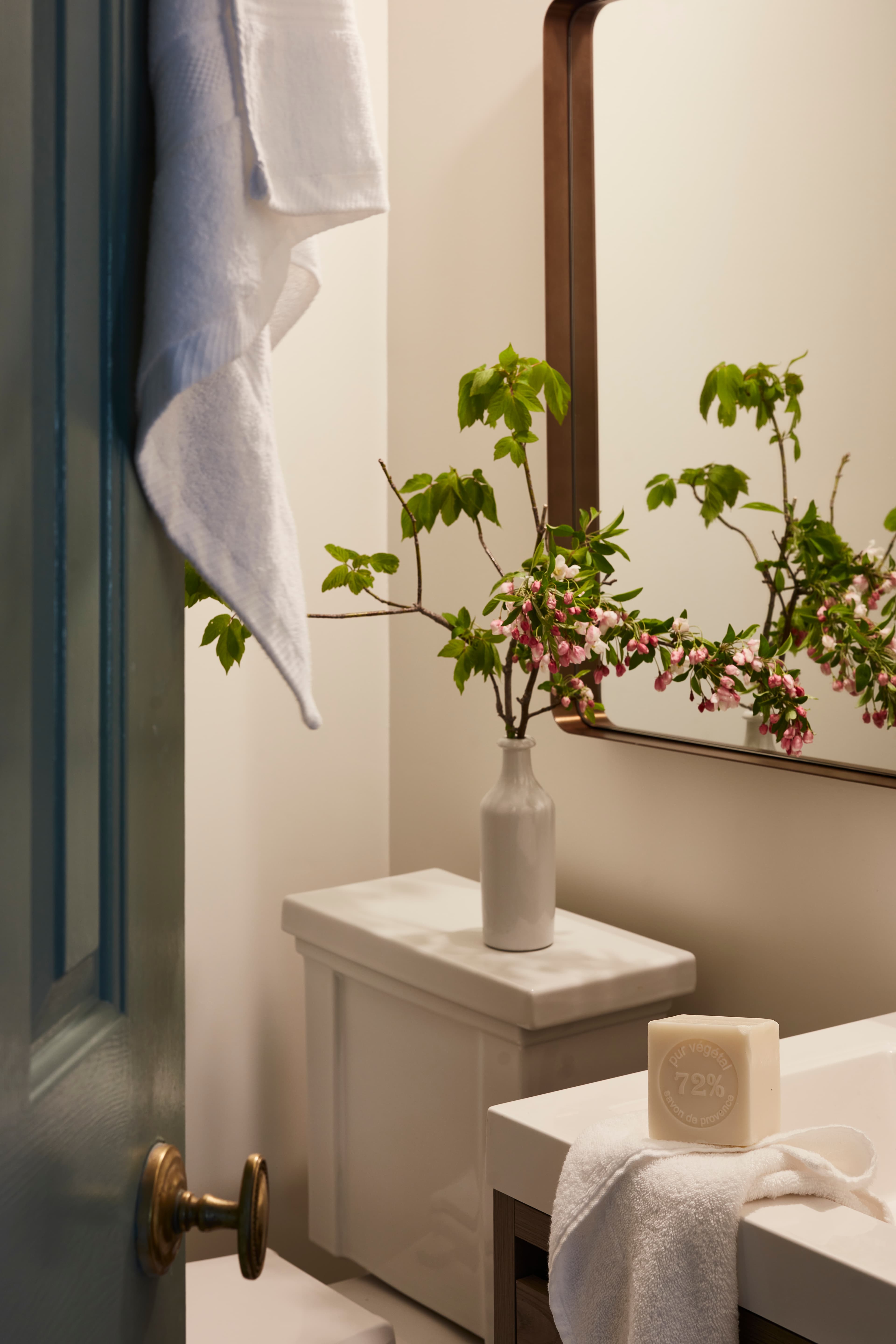 A bathroom with a white towel, a small vase with flowers, a bar of soap, and a mirror.