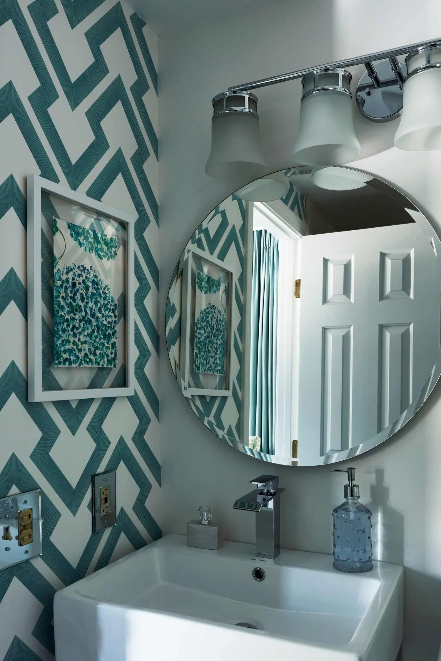 Modern bathroom with blue patterned wallpaper and round mirror.