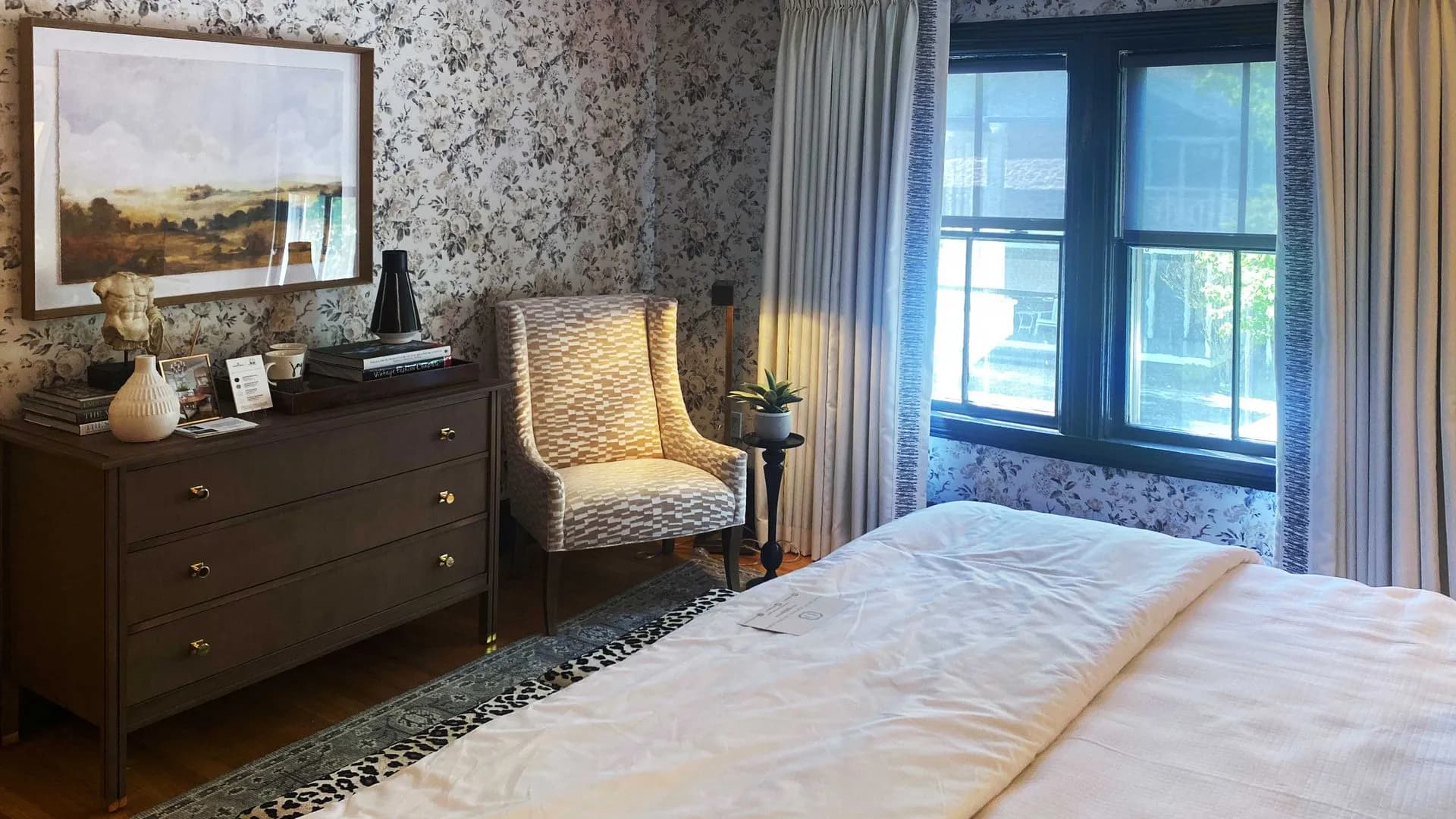 Bedroom with floral wallpaper, patterned armchair, and large framed artwork.