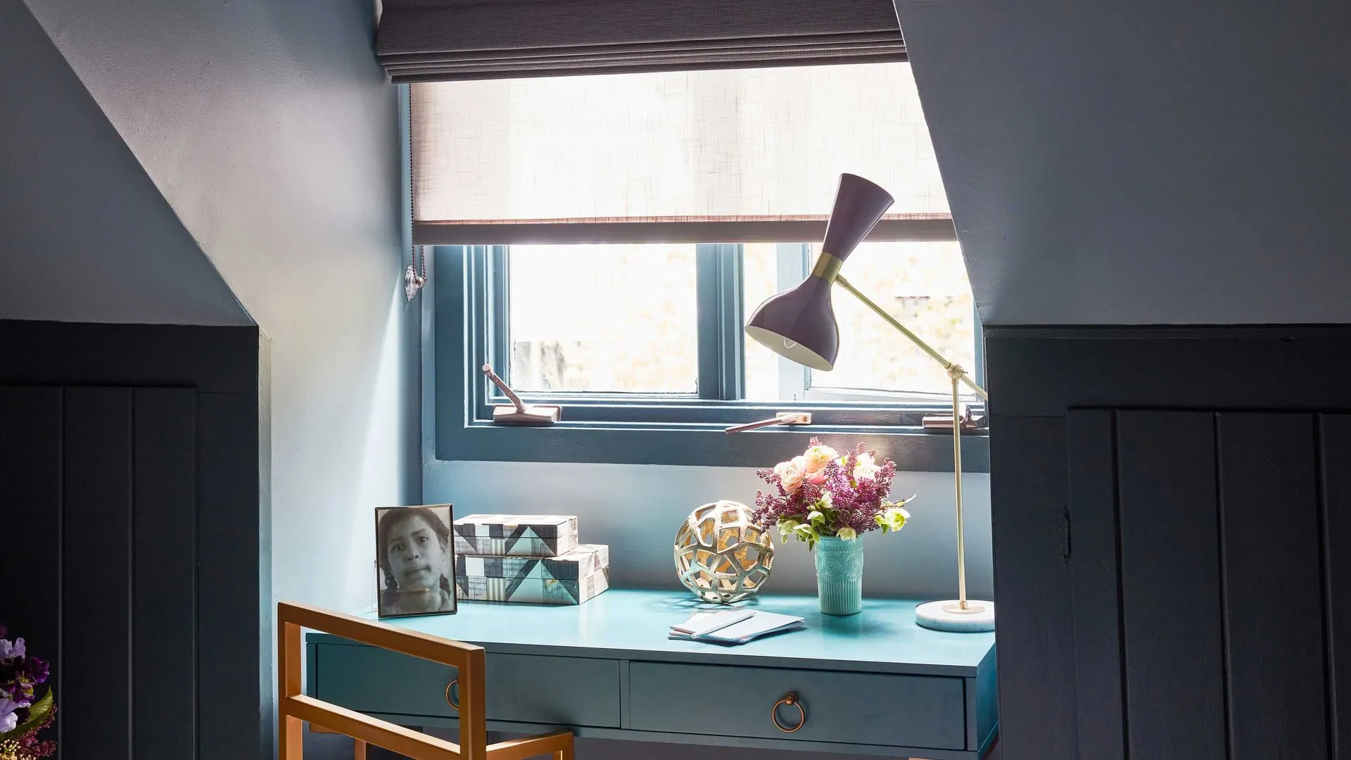 Blue study nook with desk, lamp, and window with blinds.
