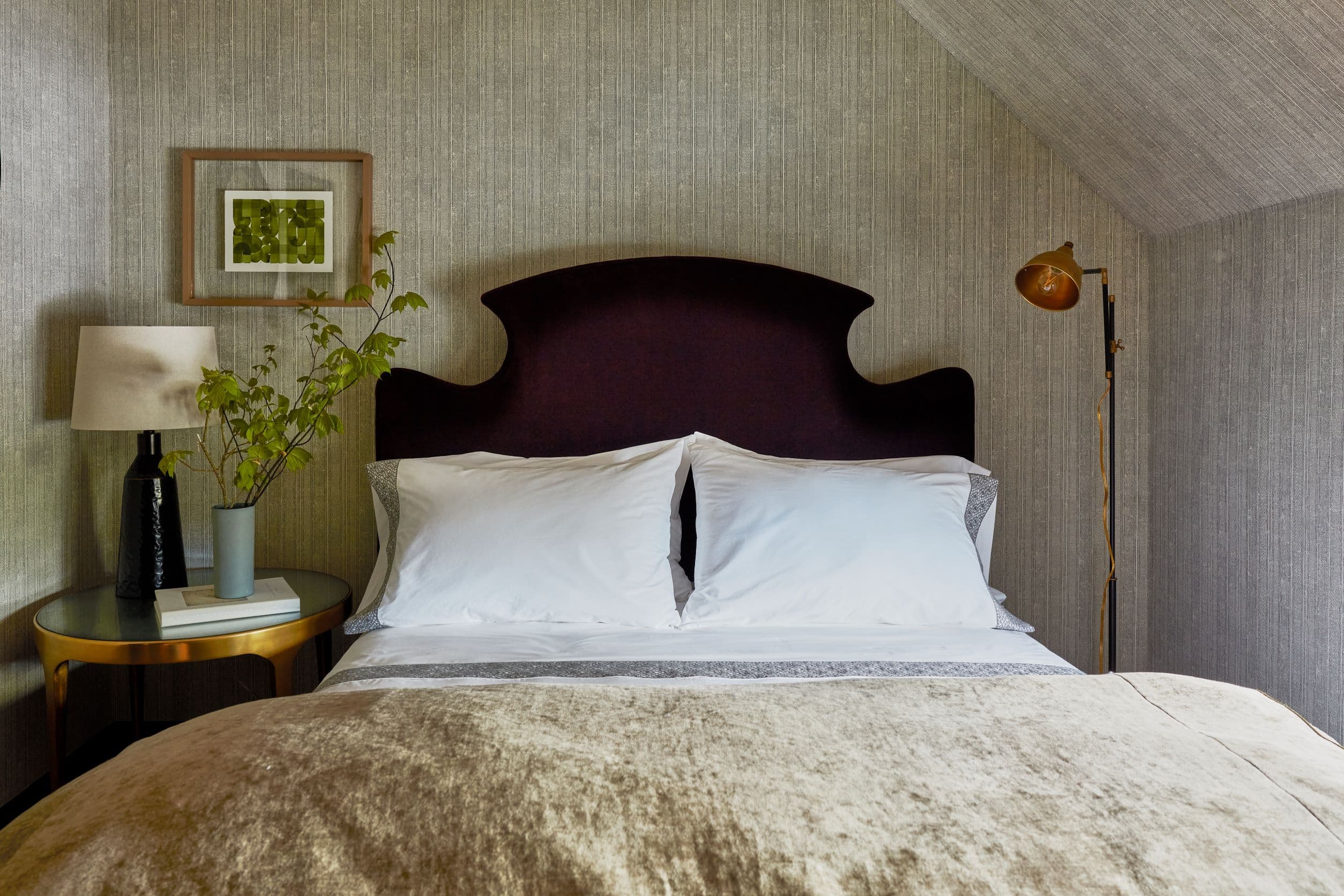 A hotel room with a made bed, side table, artwork, and lamp.