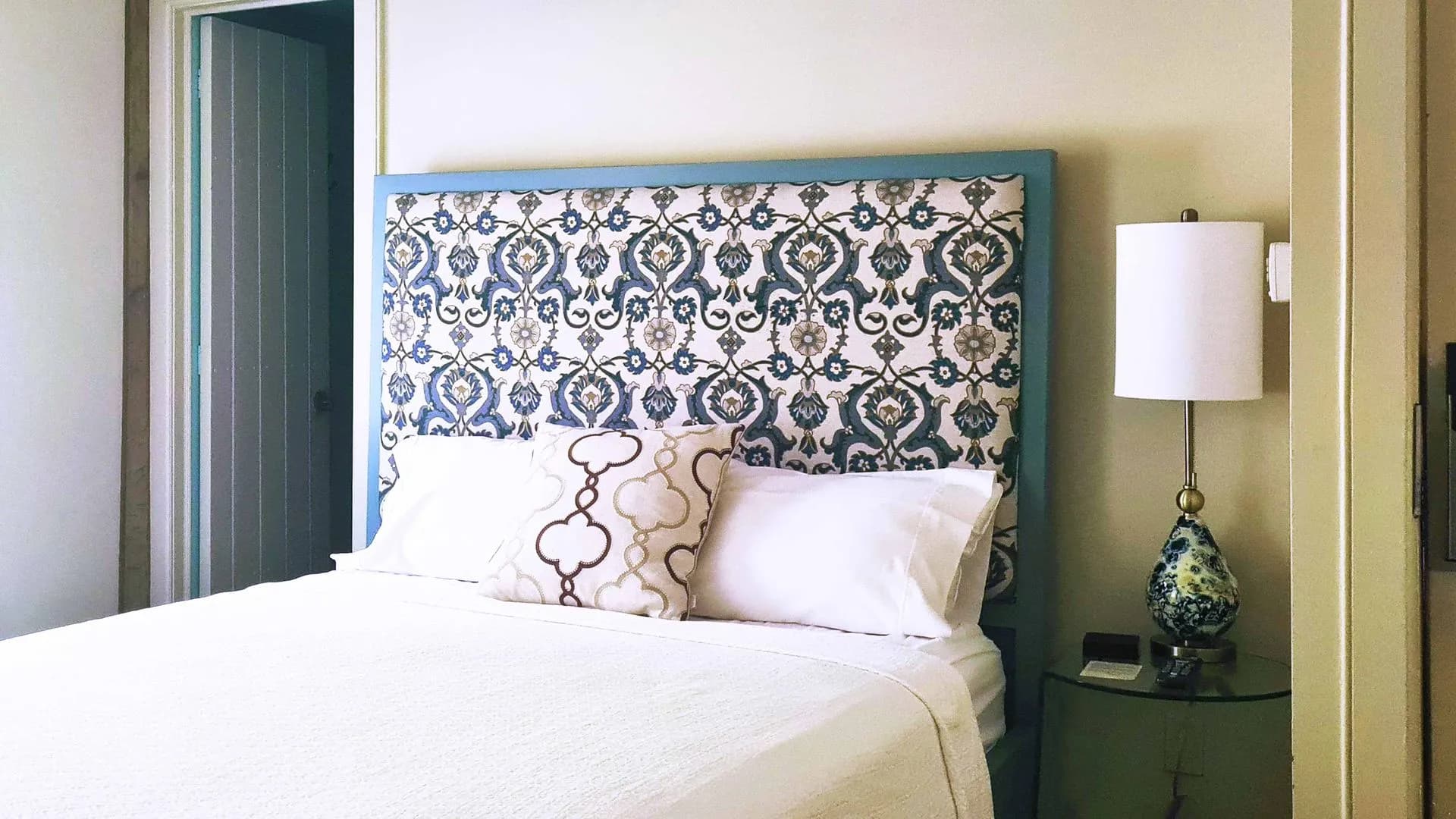 Bedroom with patterned headboard, white bedding, and bedside lamp.