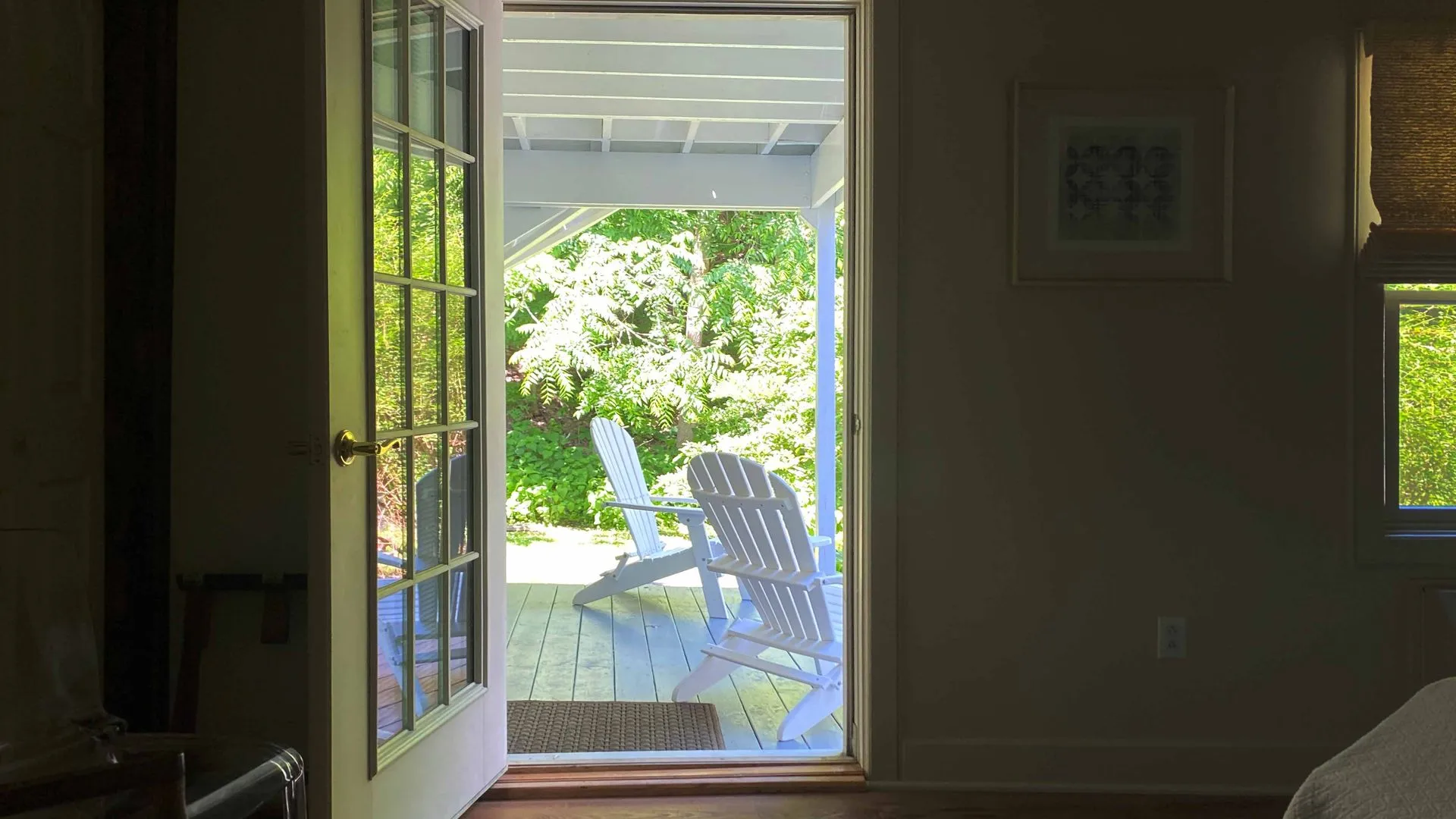 View through open French doors to a porch with two white Adirondack chairs.
