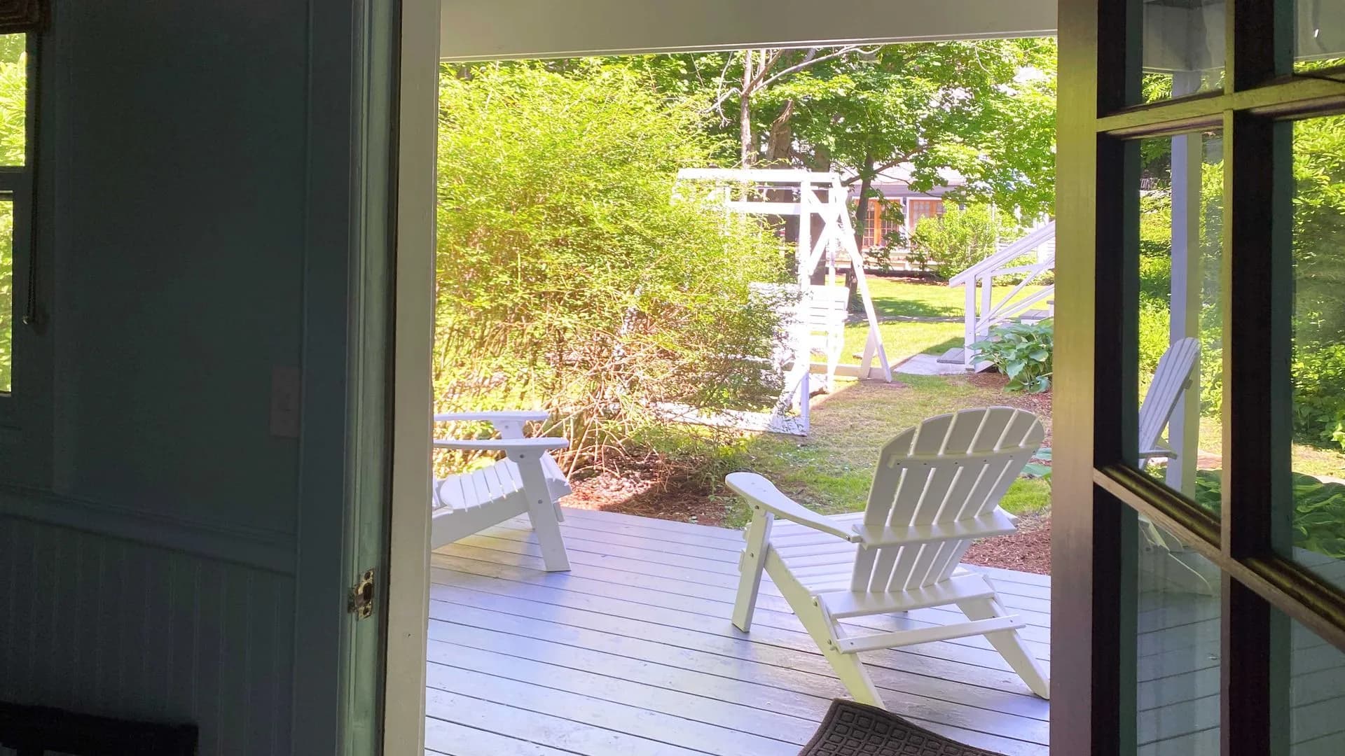 Outdoor patio with two white Adirondack chairs and a swing.
