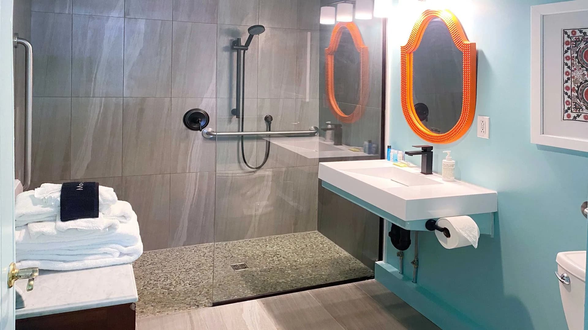 Modern bathroom with walk-in shower, floating sink, and orange accents.