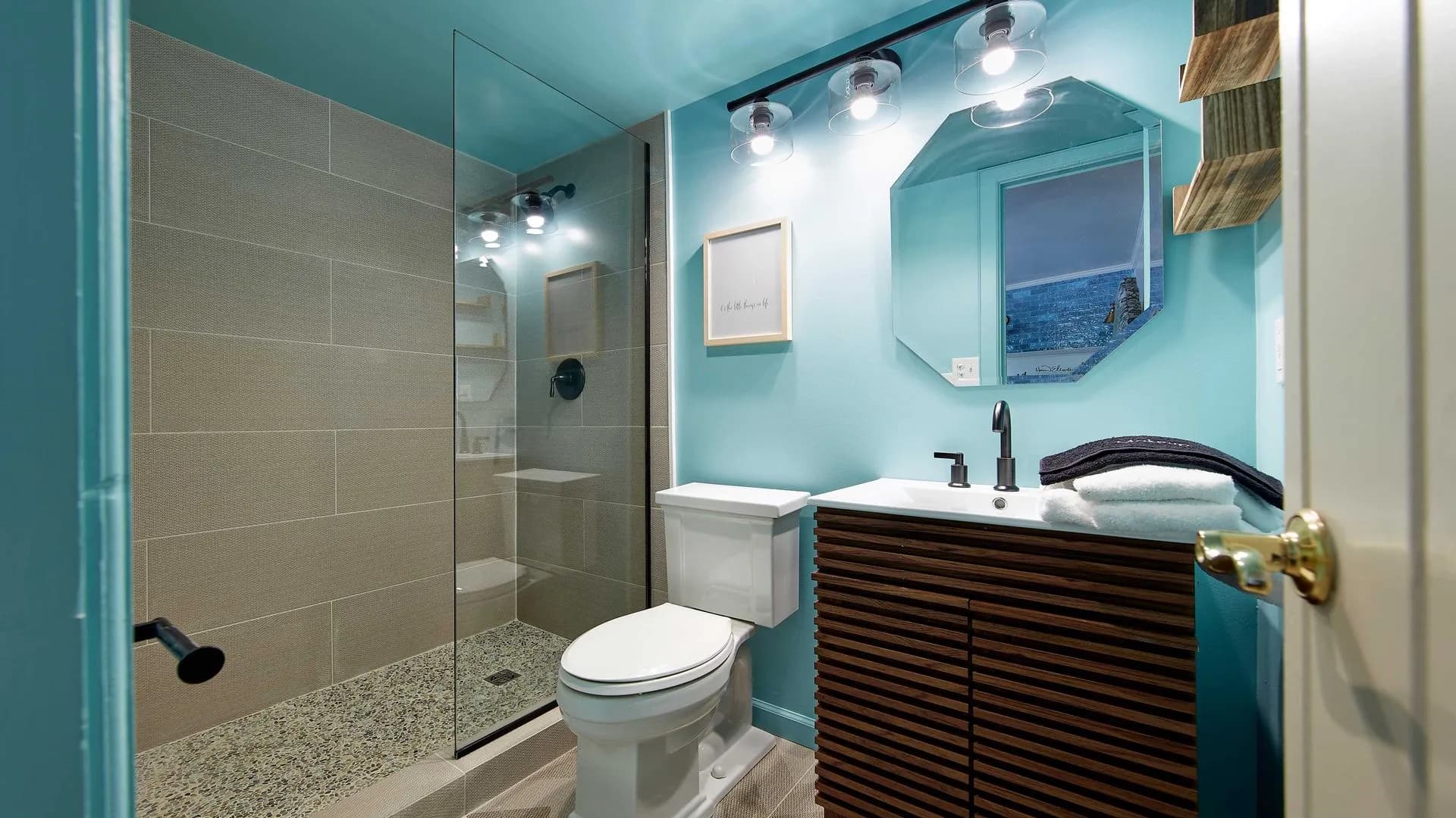 Bright vibrant bathroom blue walls, walk-in glass shower, and single toilet and vanity sink