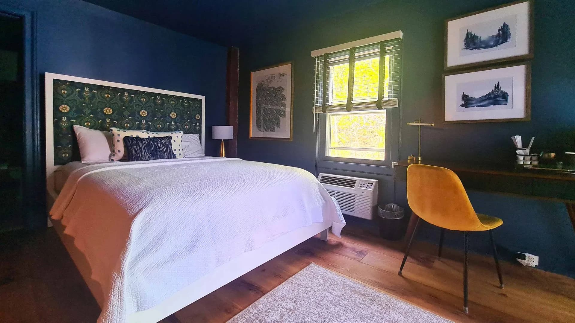 Dark, moody bedroom with blue walls, patterned headboard, and yellow chair.