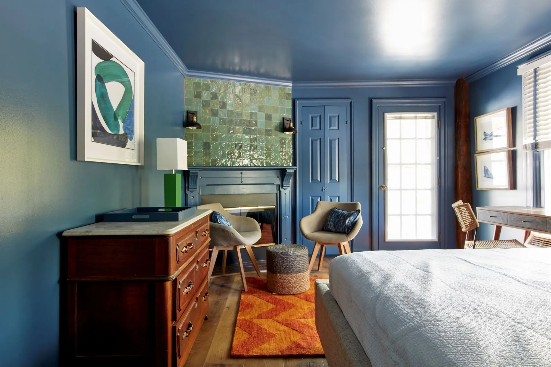 Blue bedroom with fireplace, orange rug, and two armchairs.