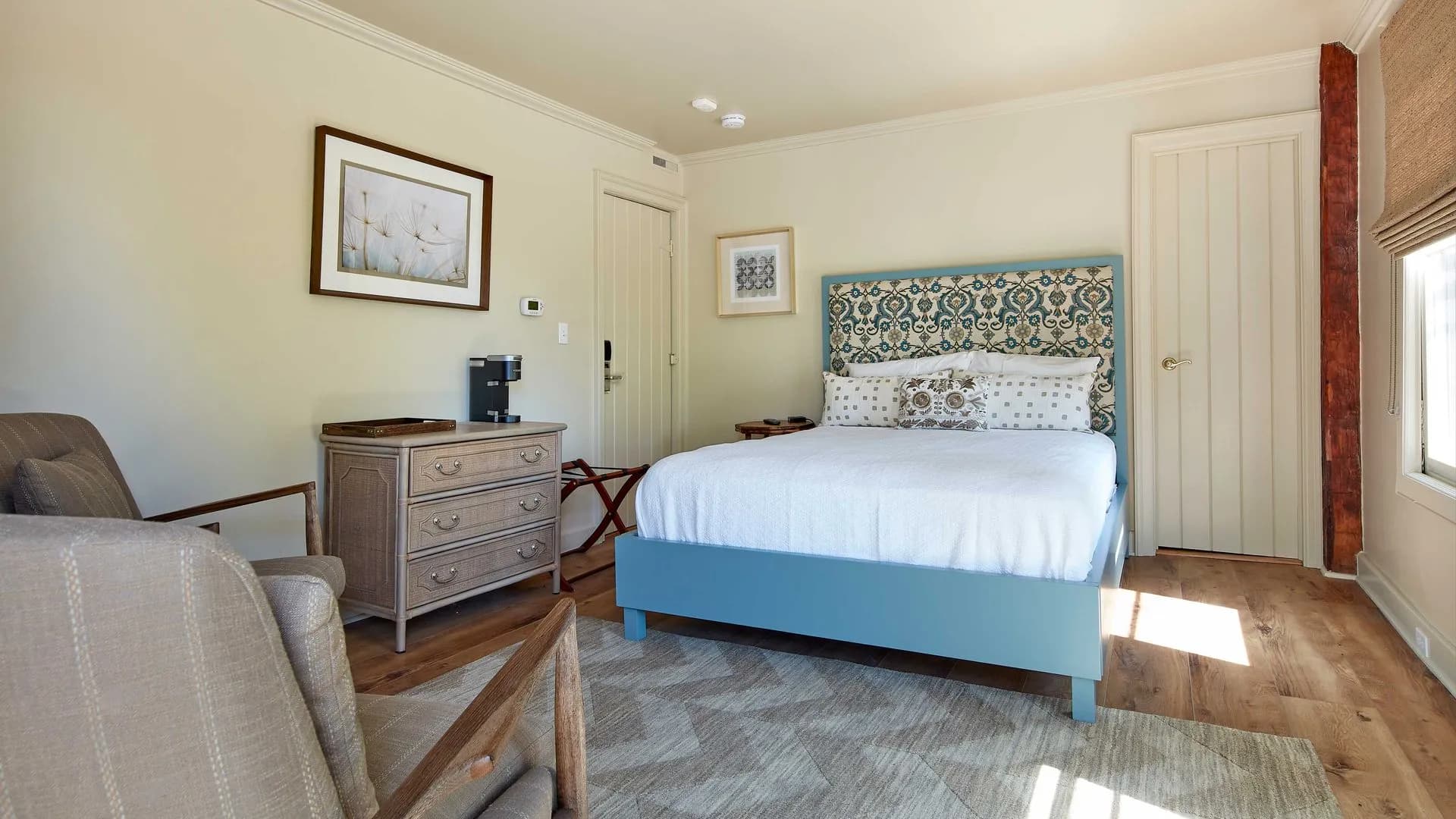 Traditional bedroom with blue headboard, neutral walls, and two armchairs.