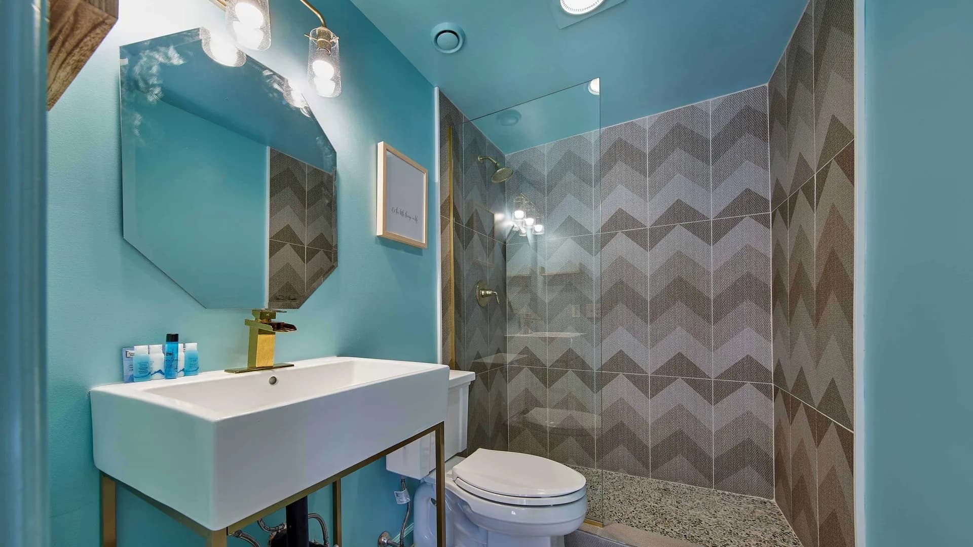 Modern bathroom with blue walls, patterned shower tiles, and unique mirror.