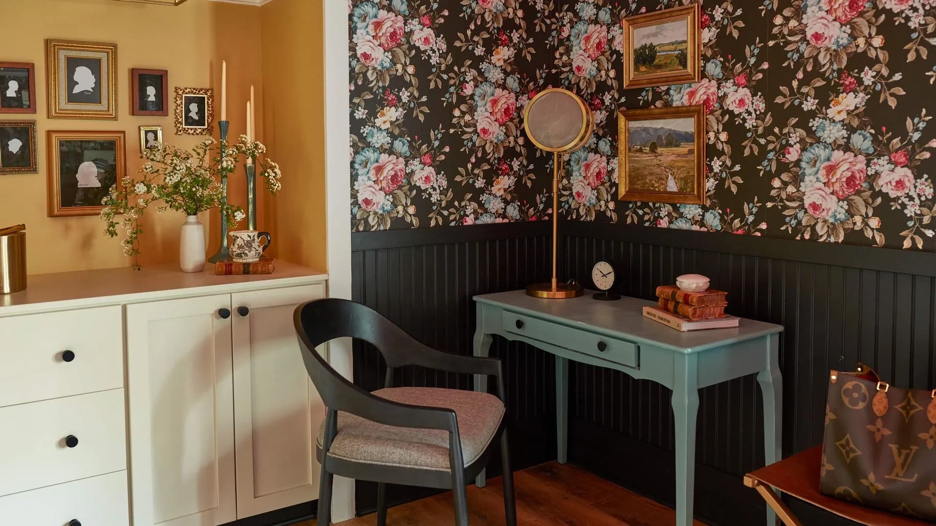 Sitting room with floral wallpaper, desk, black accent wall, and gallery wall.