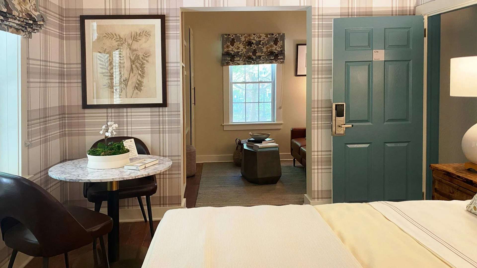 small table with chair in the left corner with view to the sitting area with a brown leather couch and stone coffee table and a blue door to exit the room