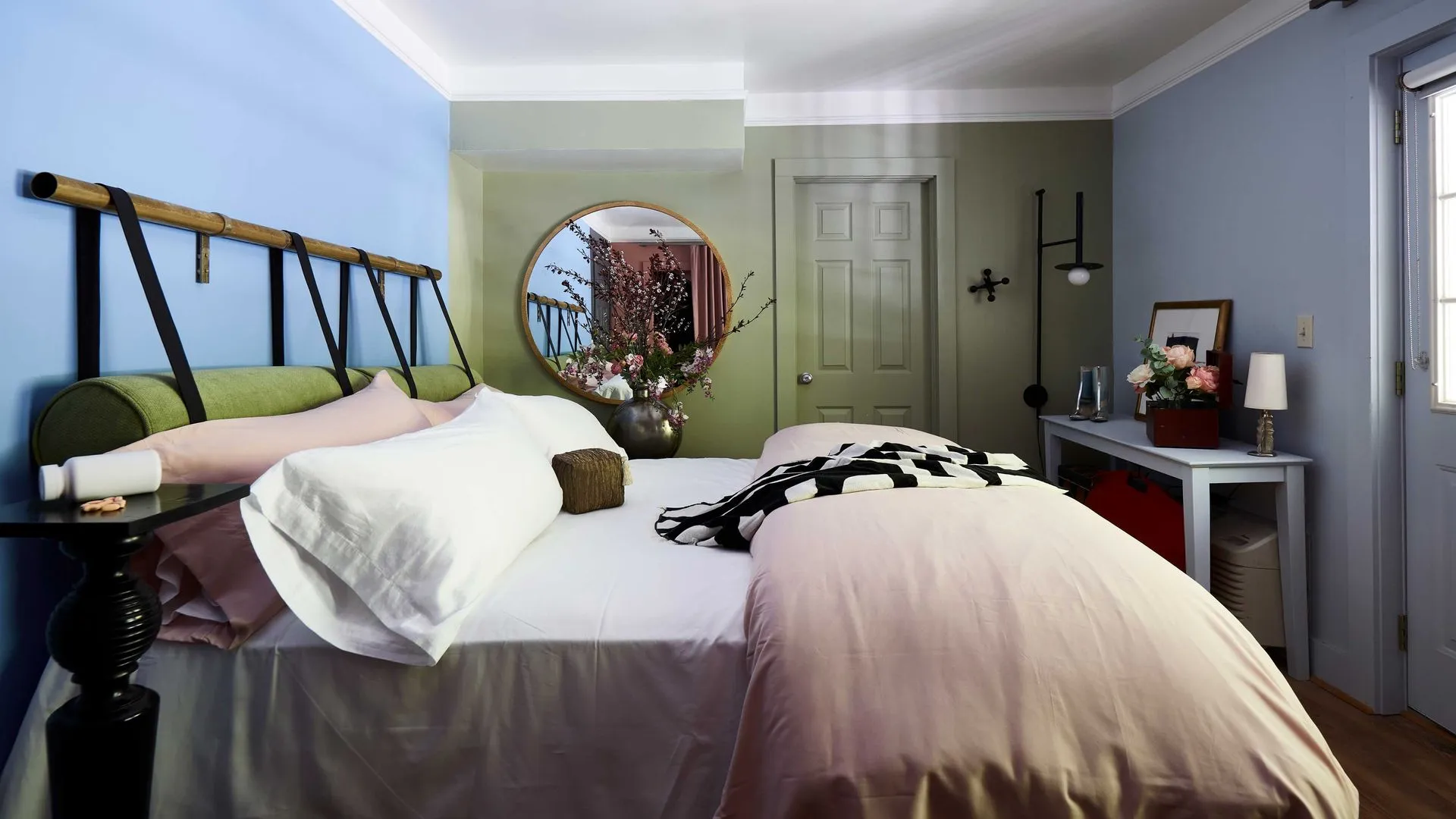 comfy bed with pink blanket at the end, a round mirror on the wall, and small desk