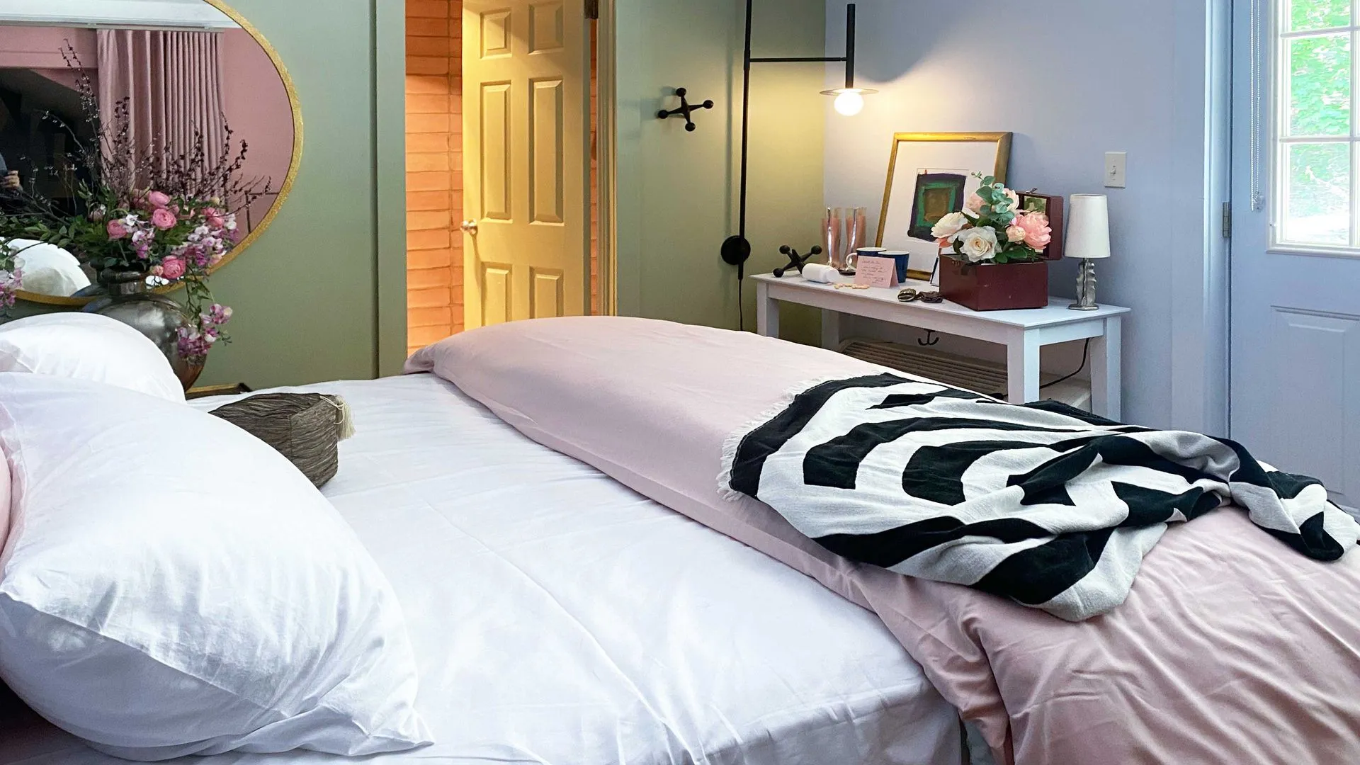 cozy bed with a pink blanket and black and white stripe throw blanket draped over the edge