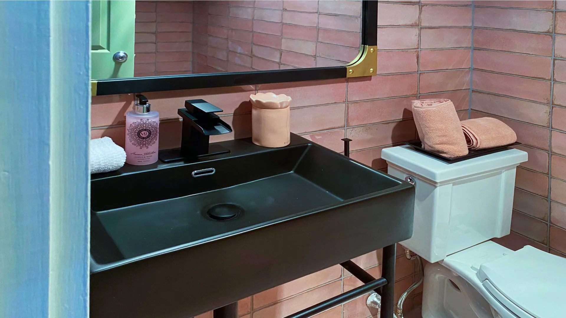 pink subway tile backsplash with a black faucet sink and single toilet