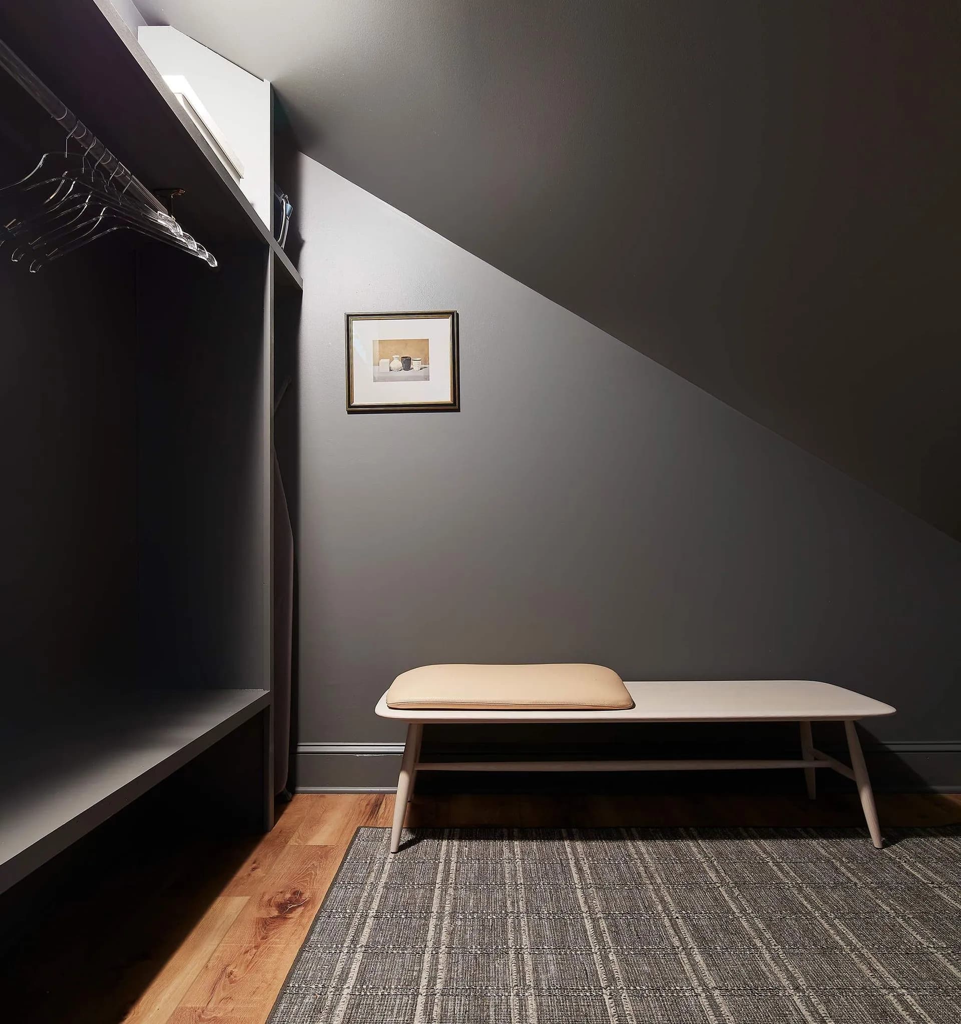 Gray walk-in closet with bench and artwork.