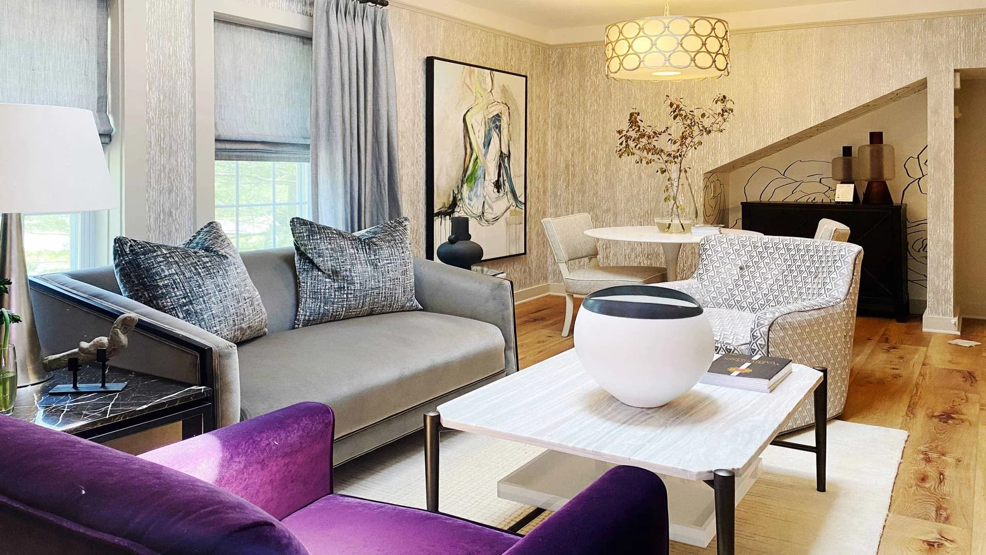 Modern sitting room with textured wallpaper, purple and gray seating, and a unique light fixture.