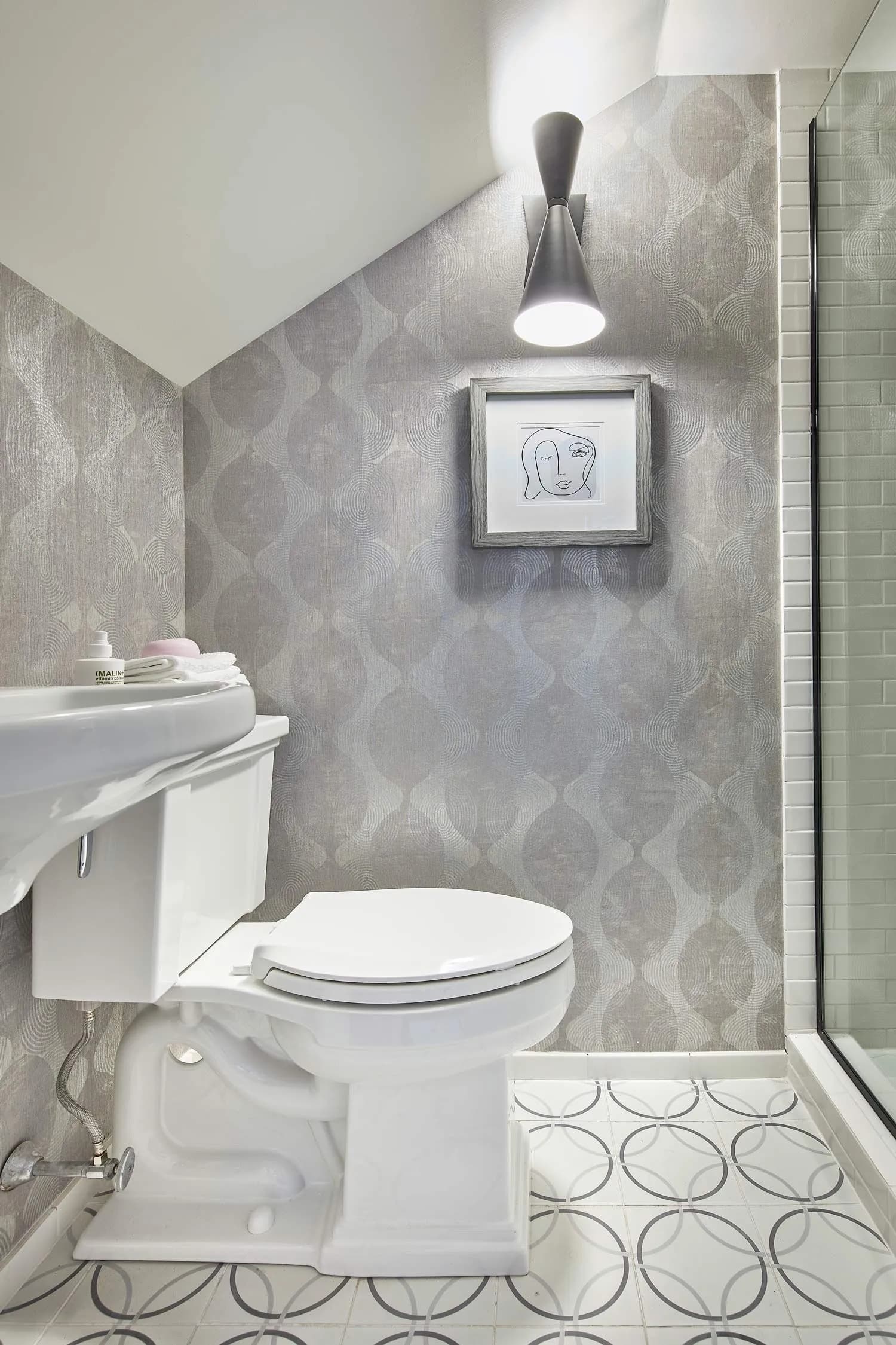 Contemporary bathroom with gray patterned wallpaper, white toilet, and glass shower.