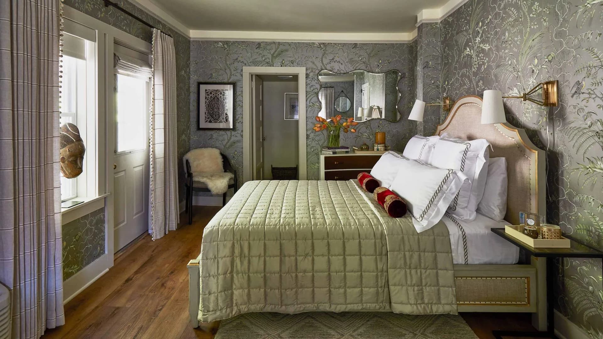 Charming bedroom with floral wallpaper, French doors, and a cozy sitting area.