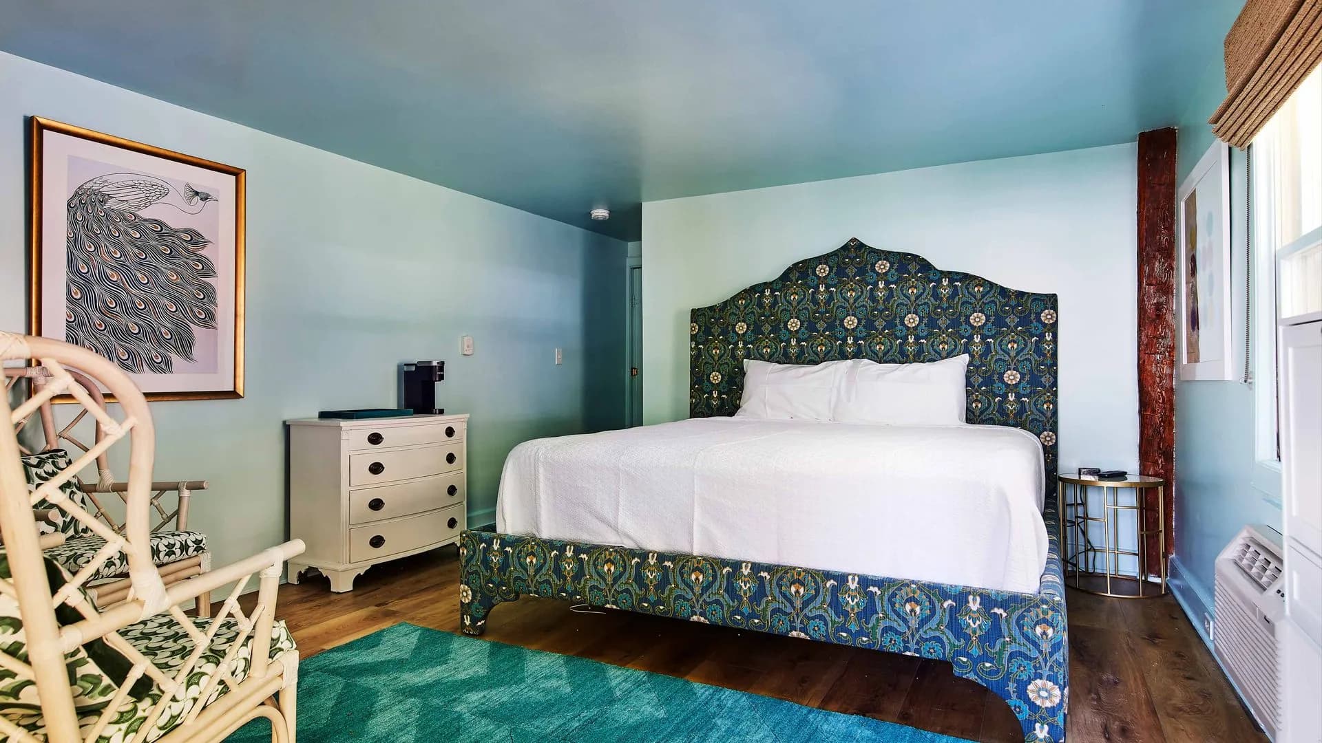 Dark blue bedframe with turquoise blue color rug and a wicker chair