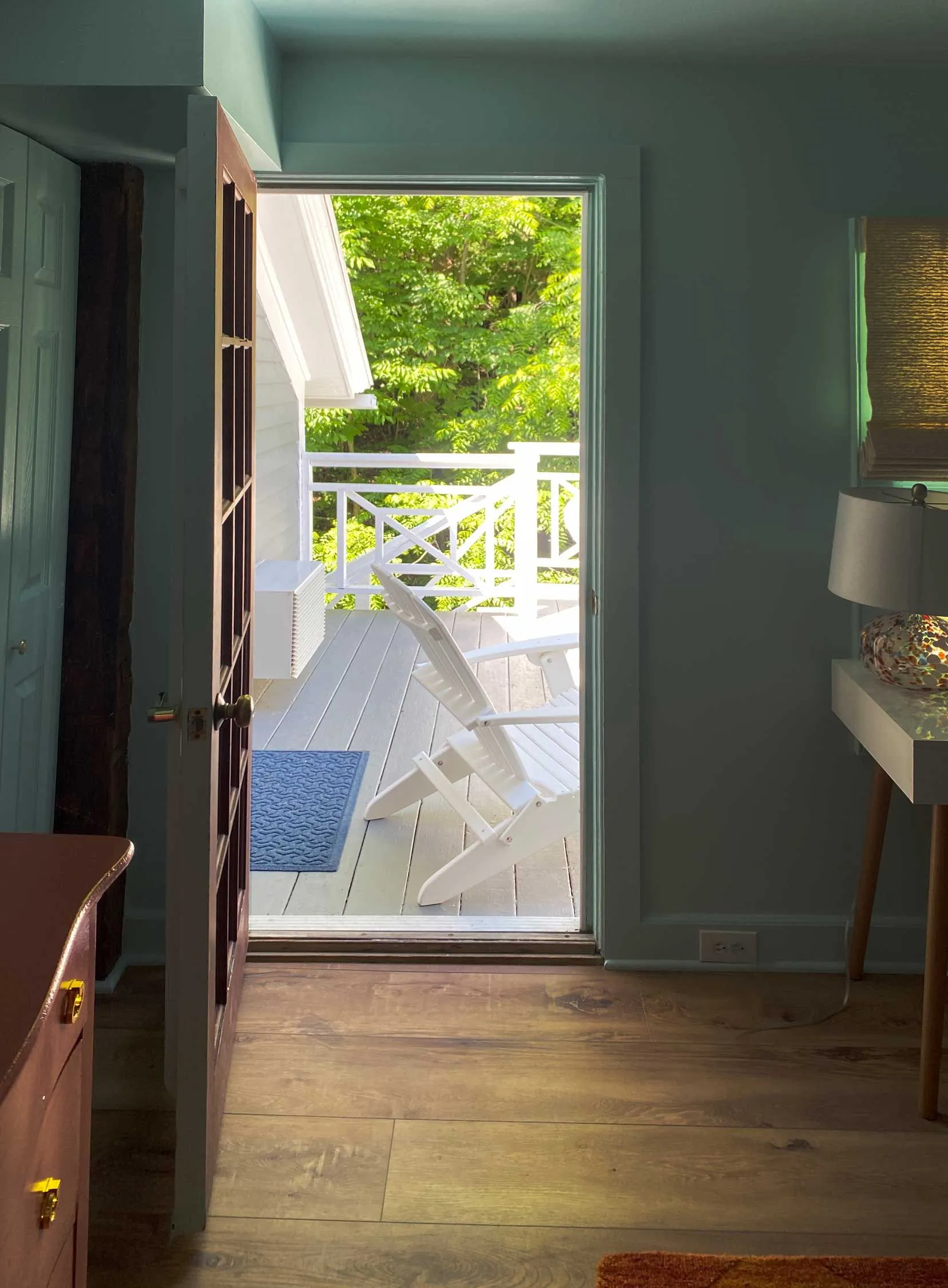 Open door leading to a balcony with white Adirondack chairs.