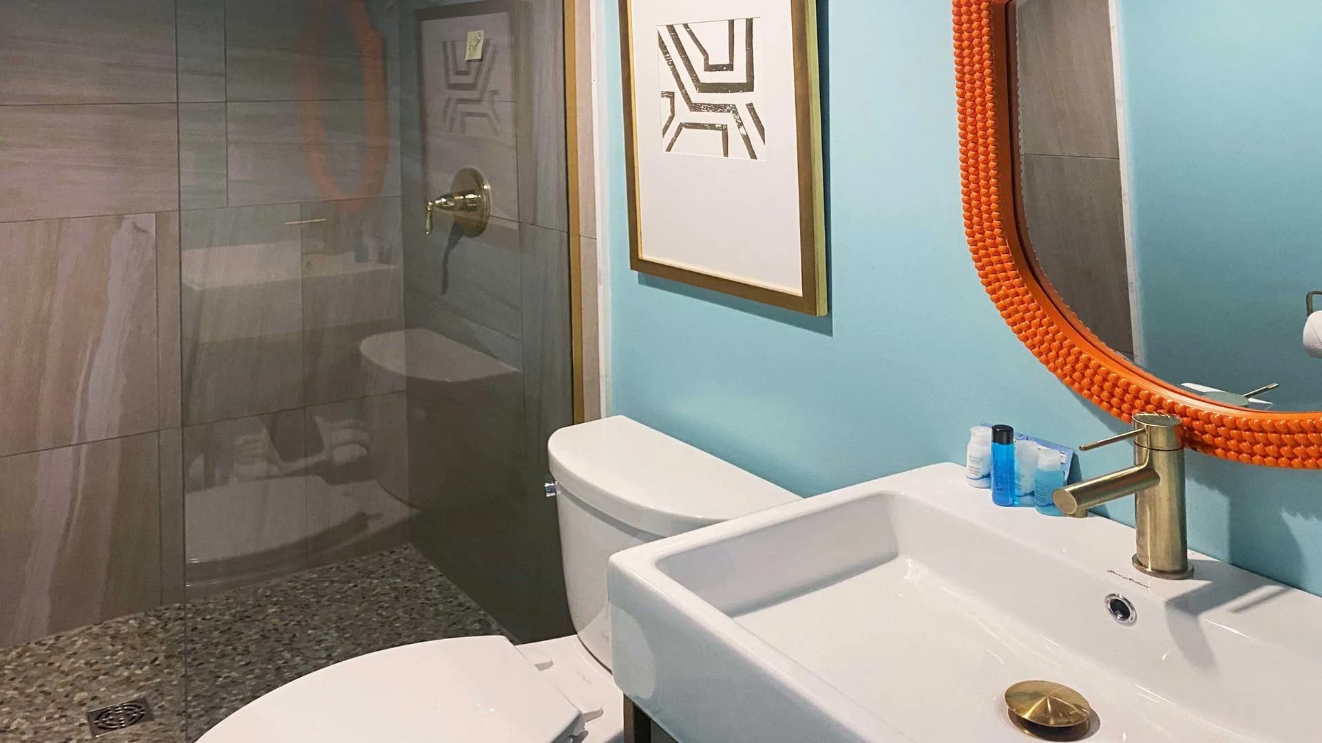 Modern bathroom with blue walls, glass shower, and orange mirror.