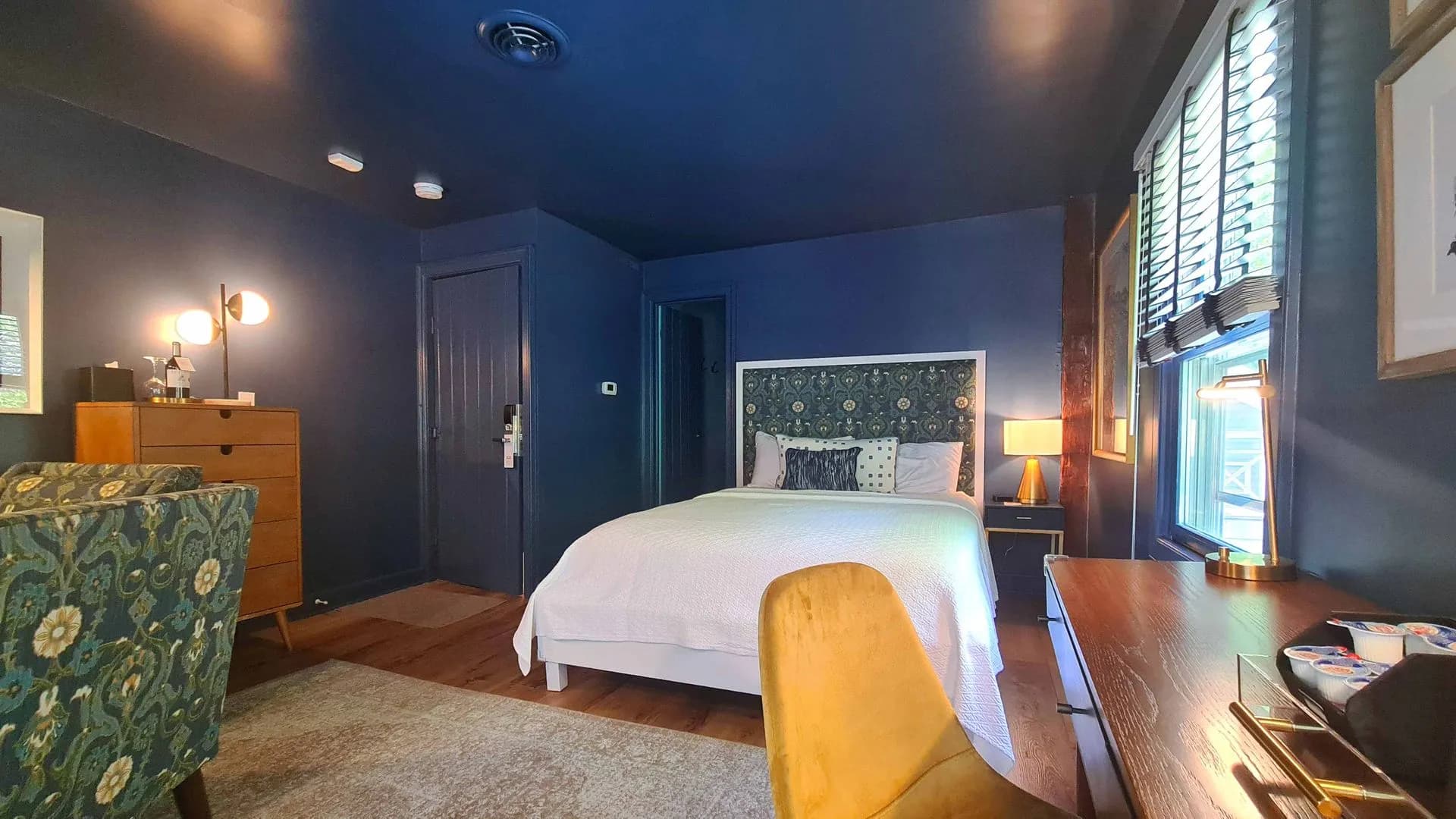 Dark blue bedroom with patterned headboard, yellow chair, and wooden desk.
