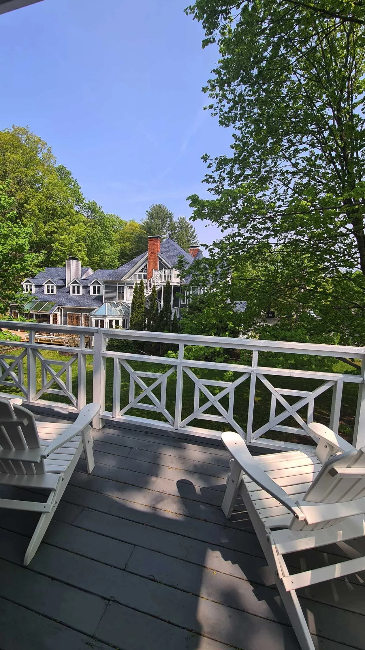 Two white Adirondack chairs on a porch overlooking a large house.