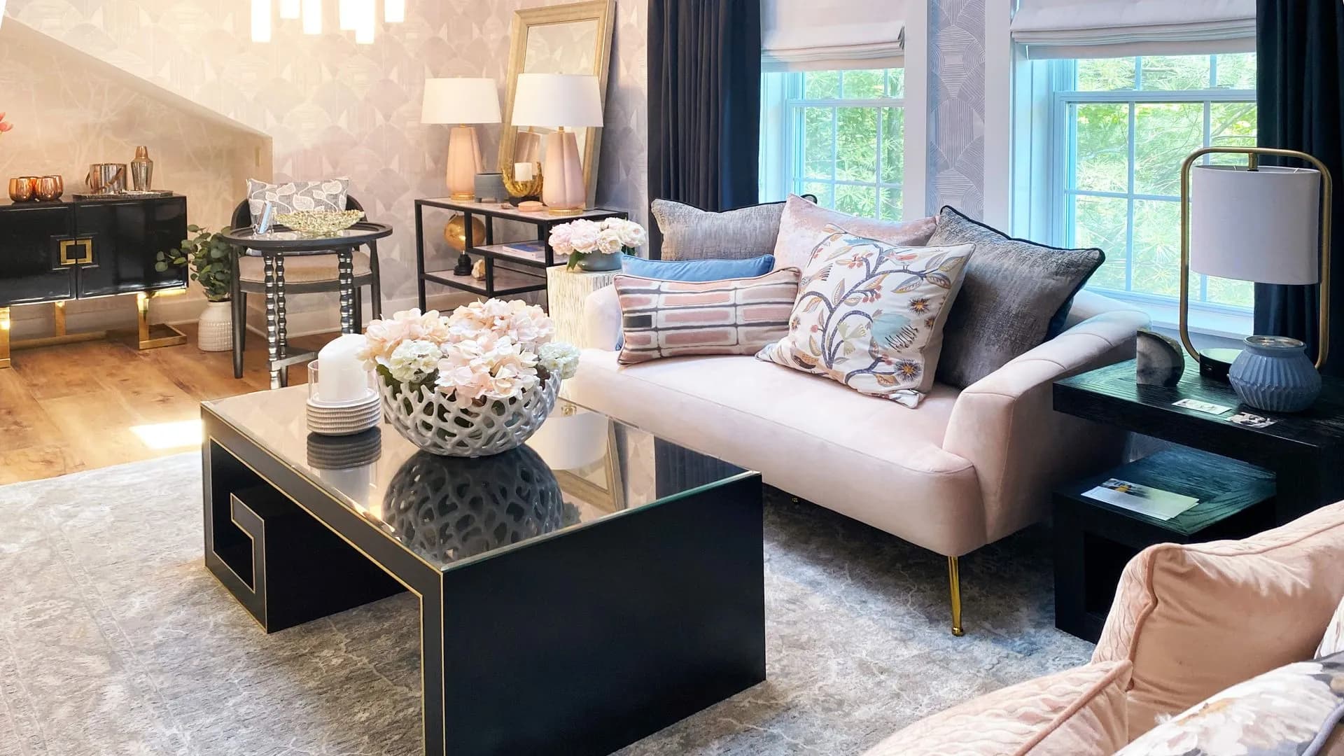 Modern living room with pink sofa, black and gold coffee table, and patterned wallpaper.