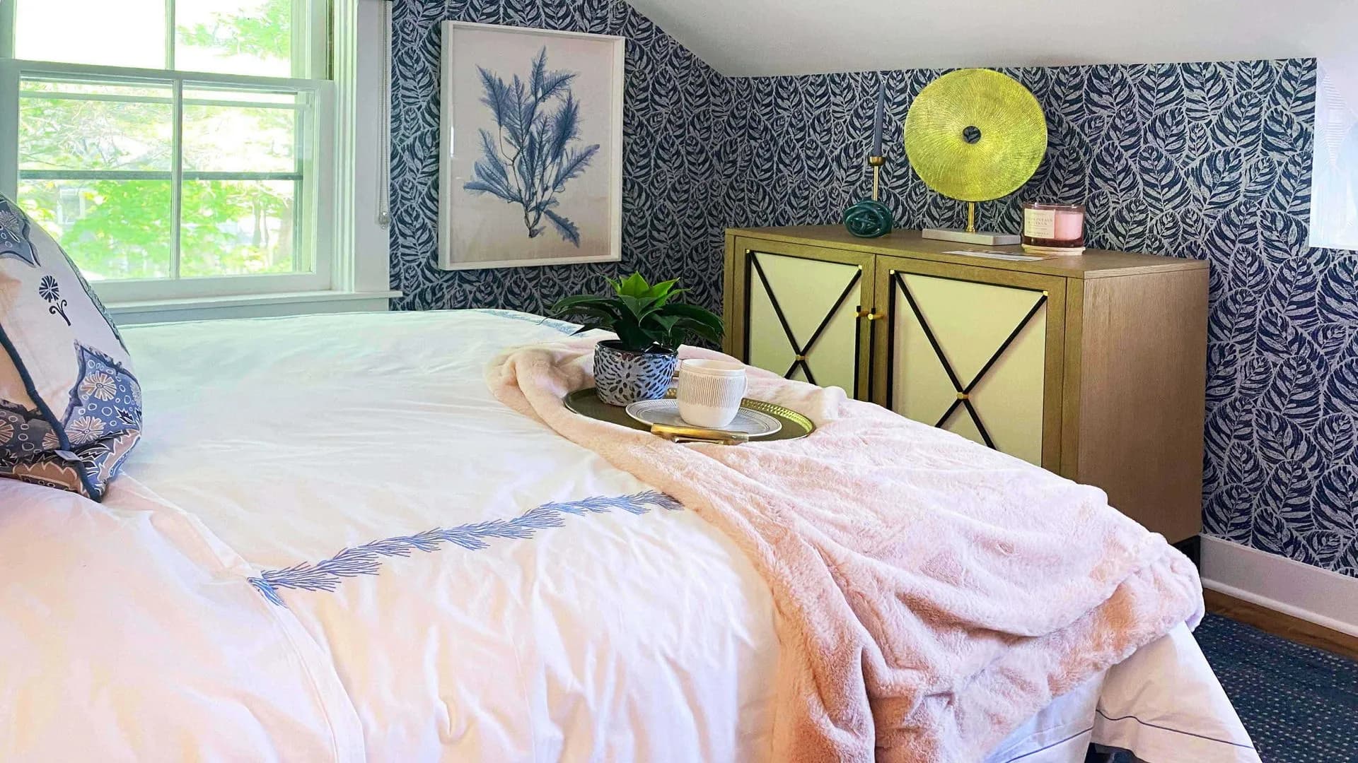 Cozy bedroom nook with patterned wallpaper, a small window, and a pink throw blanket on the bed.