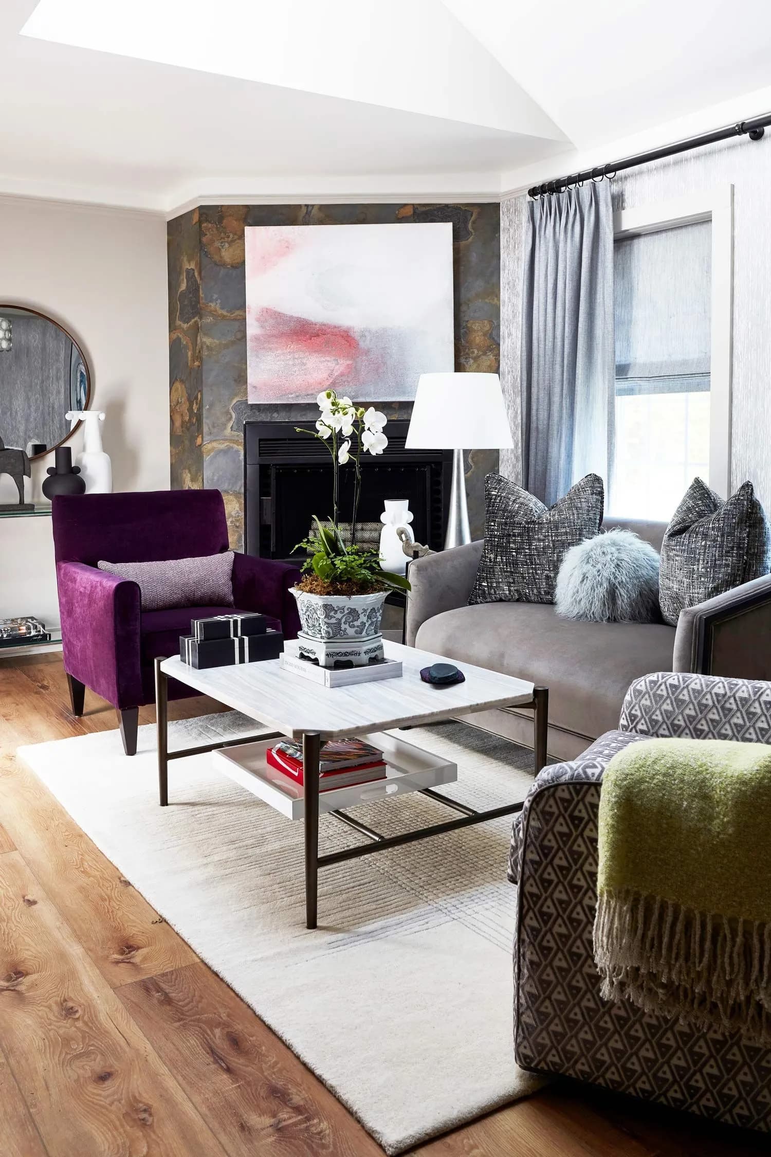 Modern living room with purple armchair, gray sofa, and stone fireplace.
