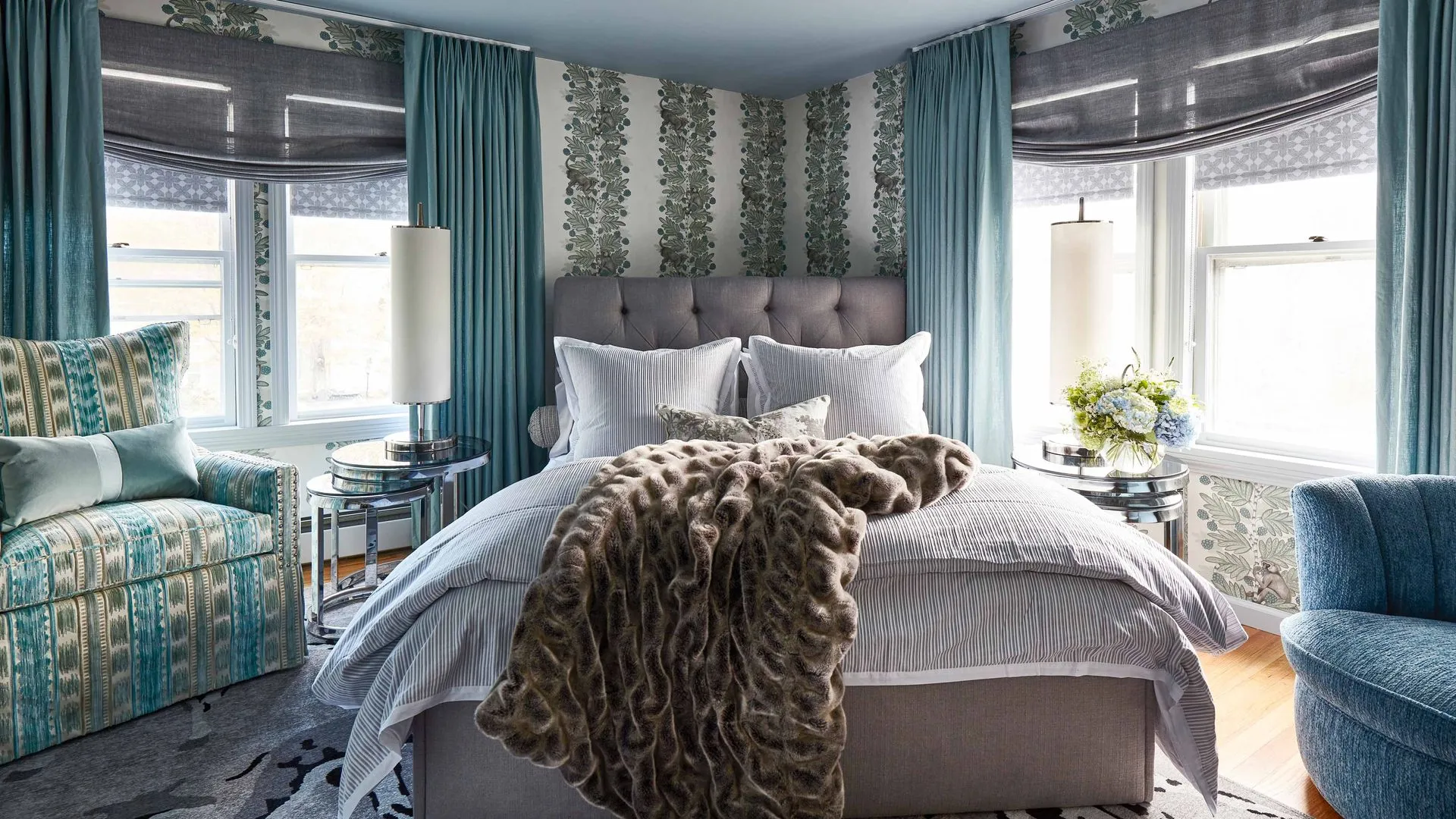 Modern bedroom with blue tones, patterned wallpaper, and a plush throw blanket.