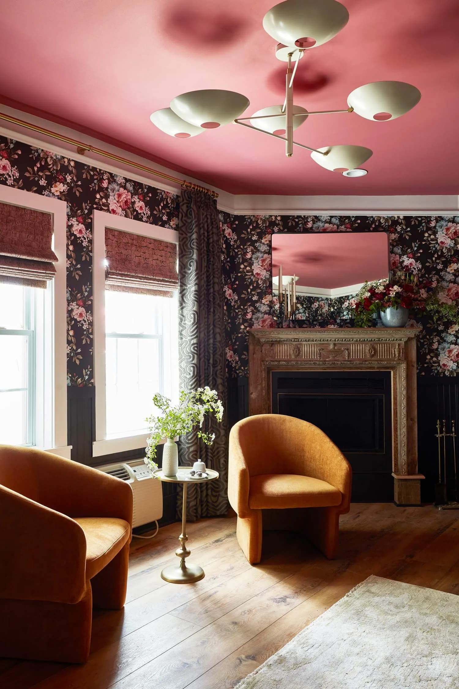 pink painted ceiling with bright flower wallpaper and 2 armchairs sitting in front of a fireplace