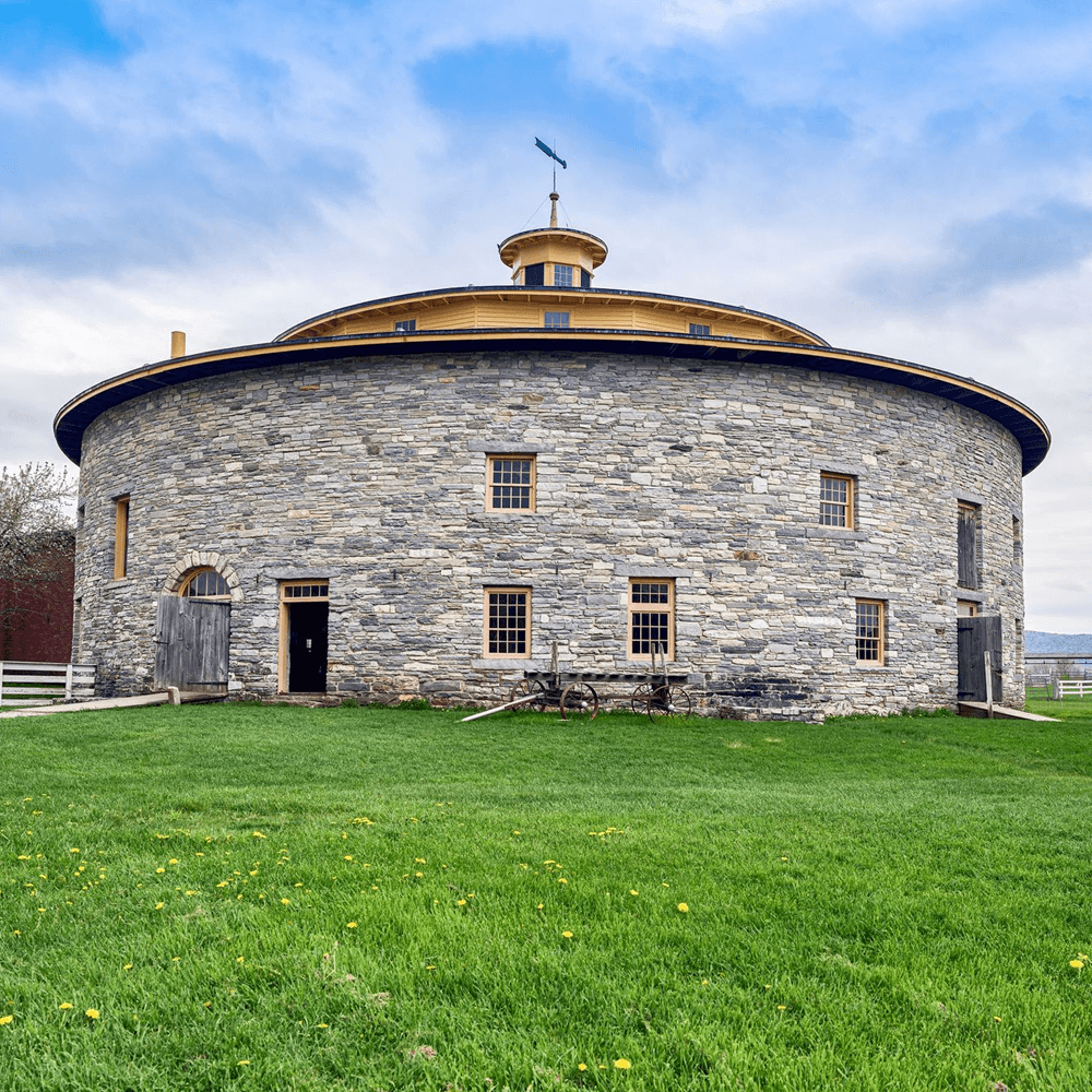 A round stone barn with a yellow roof and wooden doors surrounded by green grass.